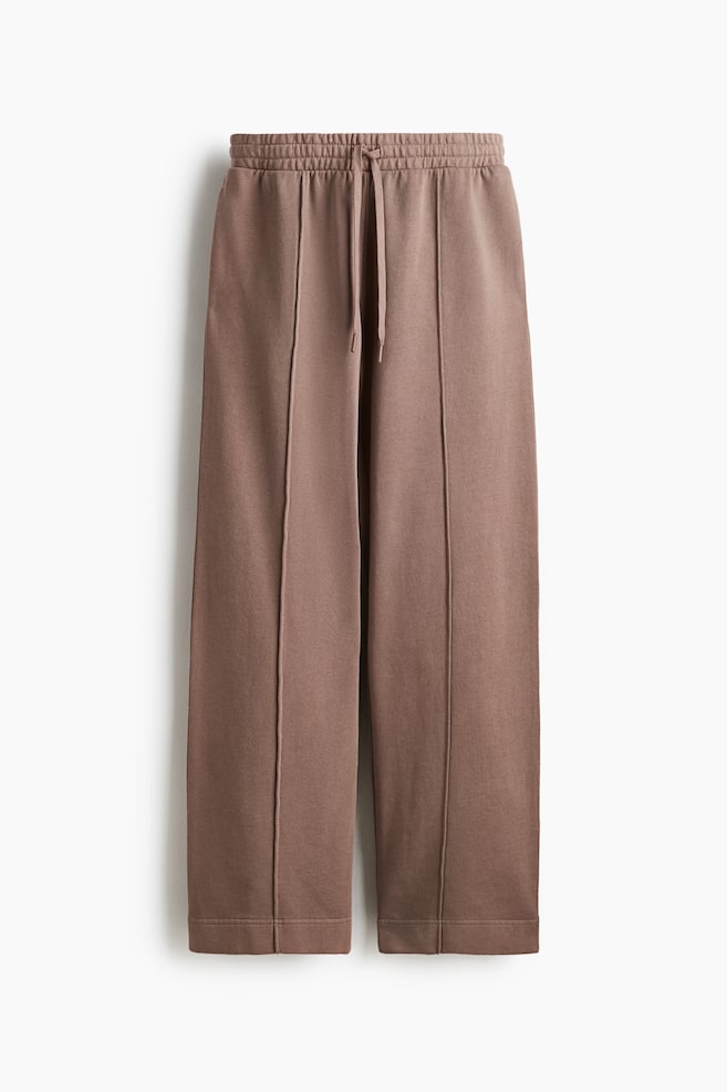 Front-facing brown sweatpants are featuring a gathered elasticated waistband with a visible drawstring, a wide-leg design with prominent vertical seams running down the front center of each leg, and plain, unribbed hems. - 1
