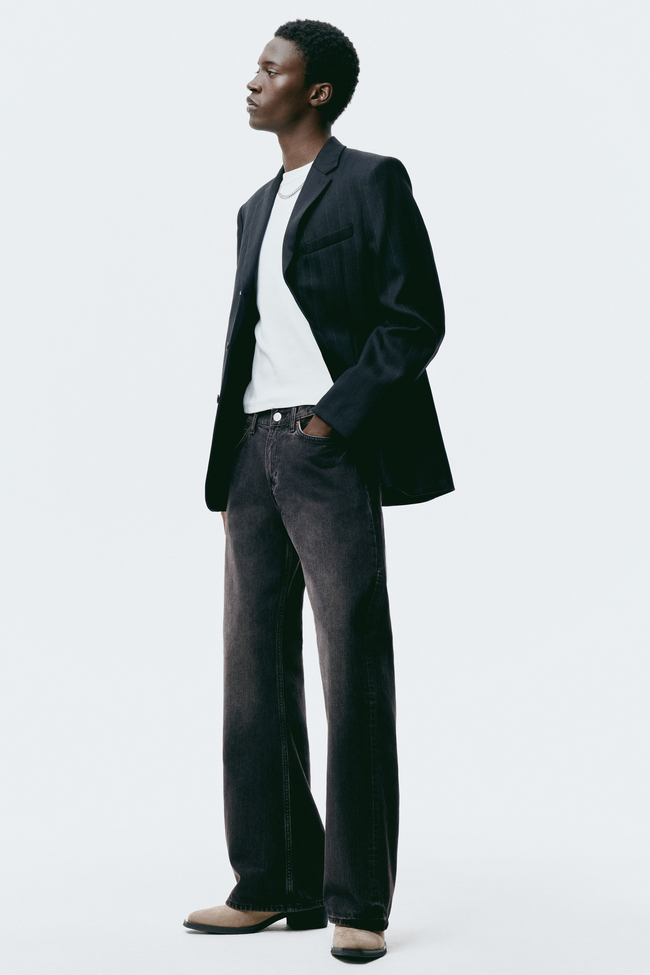 이미지 확대 보기: 검정색 핀스트라이프 블레이저를 착용하고 있으며, 오른쪽으로 약간 기울여 여유로운 핏과 노치 라펠을 드러내고 화이트 티셔츠 위에 레이어드되어 있습니다.