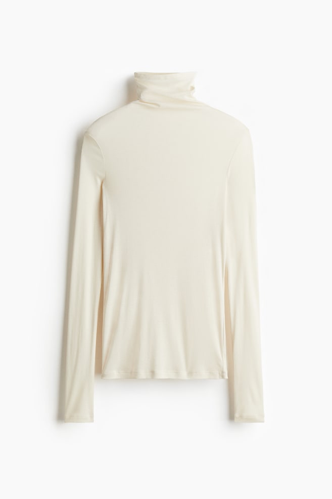 A cream-colored long-sleeve turtleneck top is shown from the back. It is featuring a high, folded neck and a smooth, fitted appearance. - 1