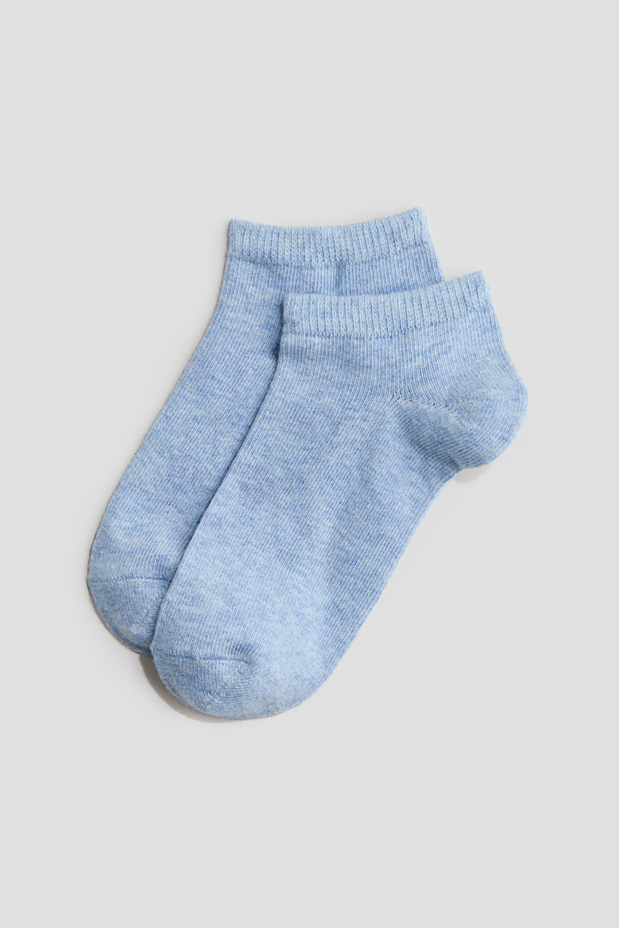 Größeres Bild ansehen: Ein Paar hellblaue Knöchelsocken liegt flach, wobei ein Socken teilweise den anderen überlappt. Die Socken zeichnen sich durch eine feinstrukturierte Strickart und gerippte Bündchen am Abschluss aus.