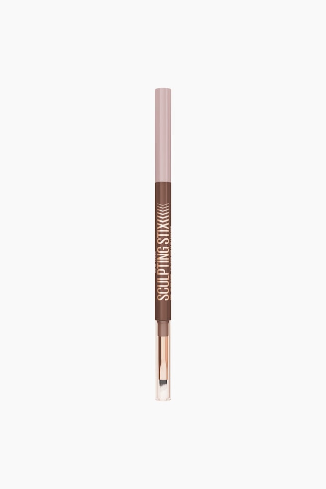 En tosidet sculpting stick står lodret og vender direkte fremad. Den har en lyserød øverste sektion og en mørkebrun nederste sektion med rosaguld-teksten "SCULPTING STIX". Den ene ende afslører en mørkebrun make-upstift, mens den modsatte ende viser en blending-børste med hvide børstehår under en gennemsigtig hætte. - 1
