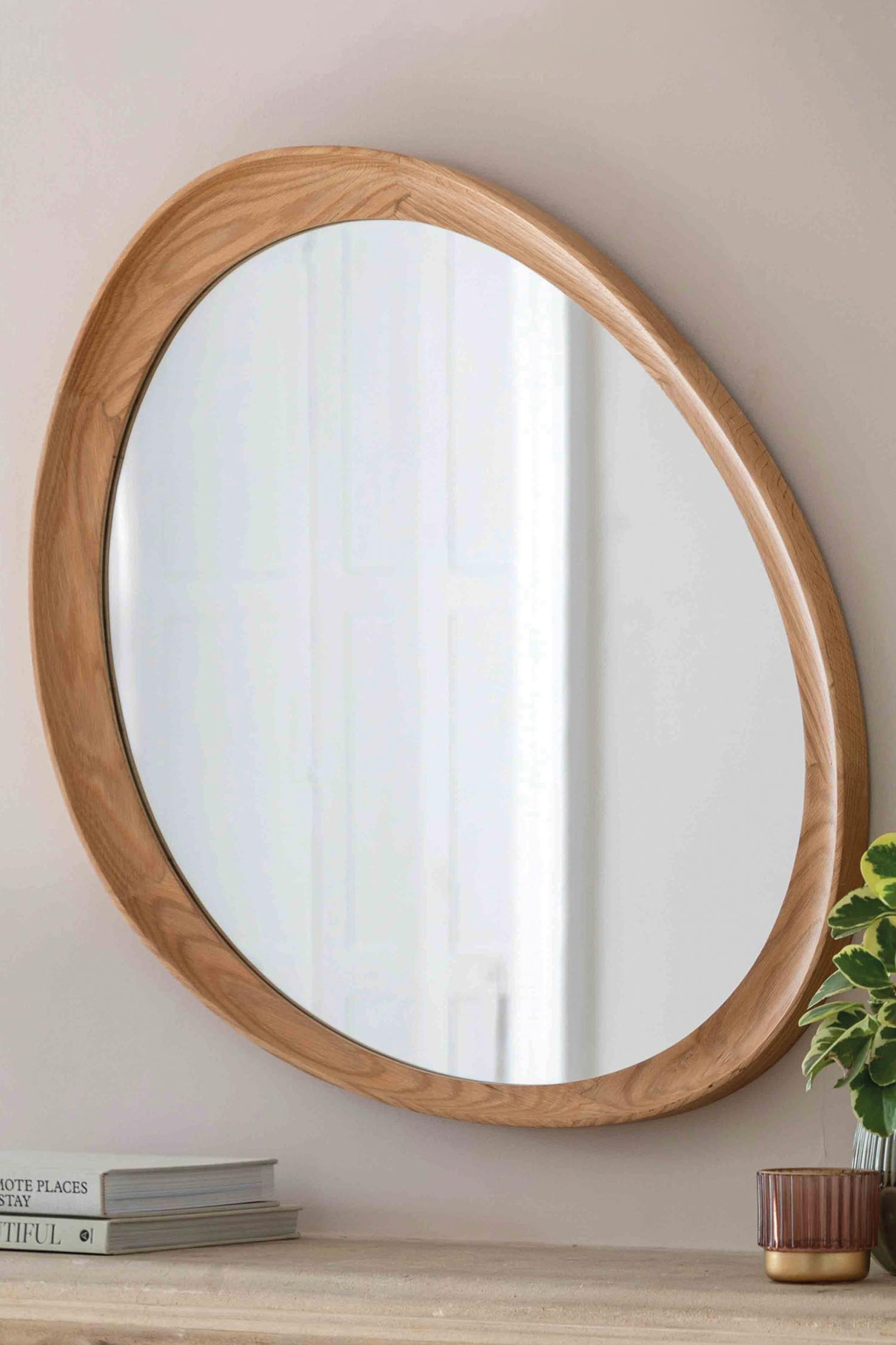View larger image: A mirror featuring an irregular, organic oval shape. It is framed by a thick, light-toned wooden border with a visible grain, curving outwards from the reflective surface.