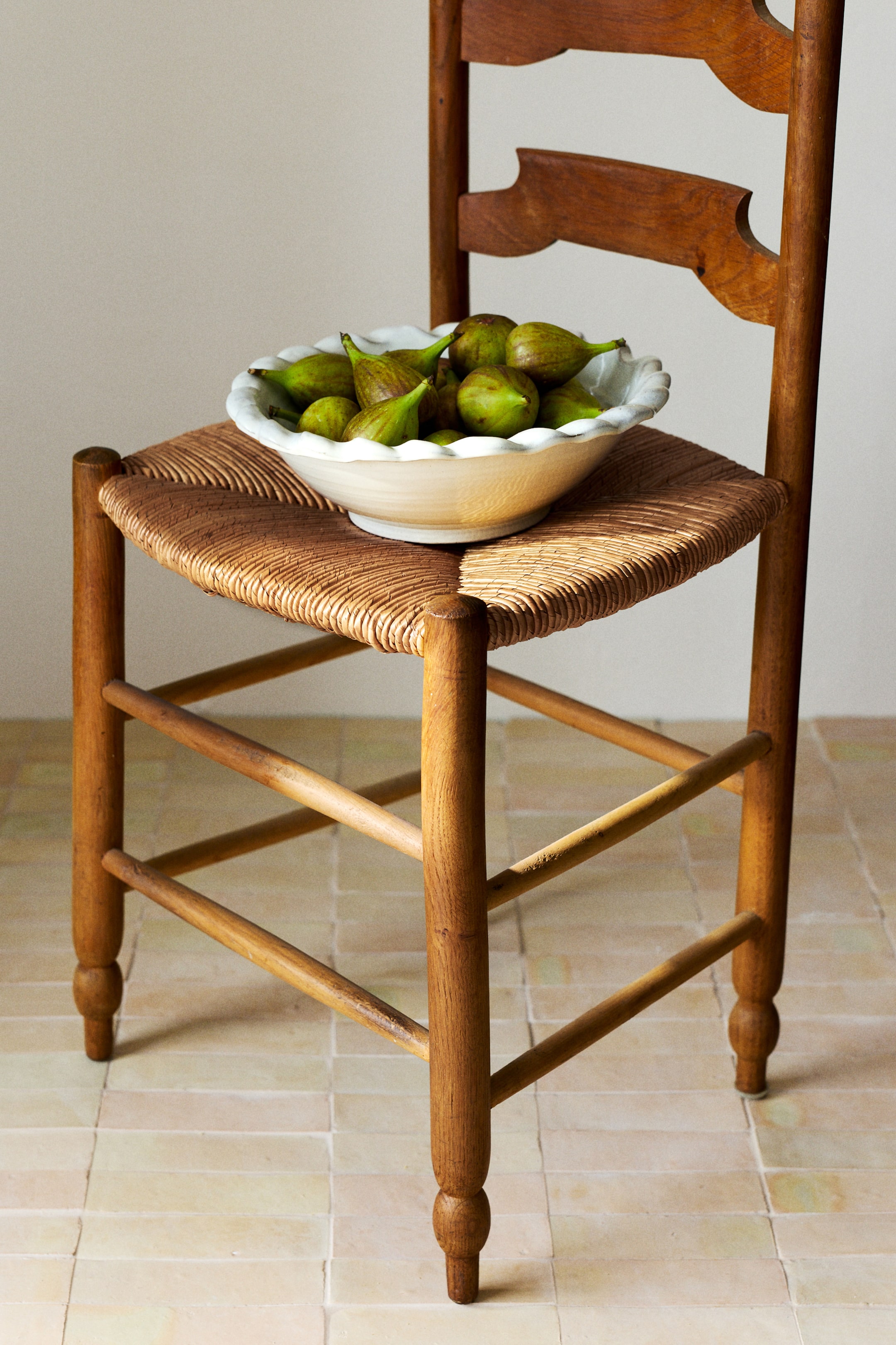 Agrandir l'image: Des figues vertes remplissent un bol en céramique blanc à bord cannelé, vu sous un angle légèrement surélevé. Les figues présentent diverses nuances de vert et de brun, certaines apparaissant légèrement ridées.