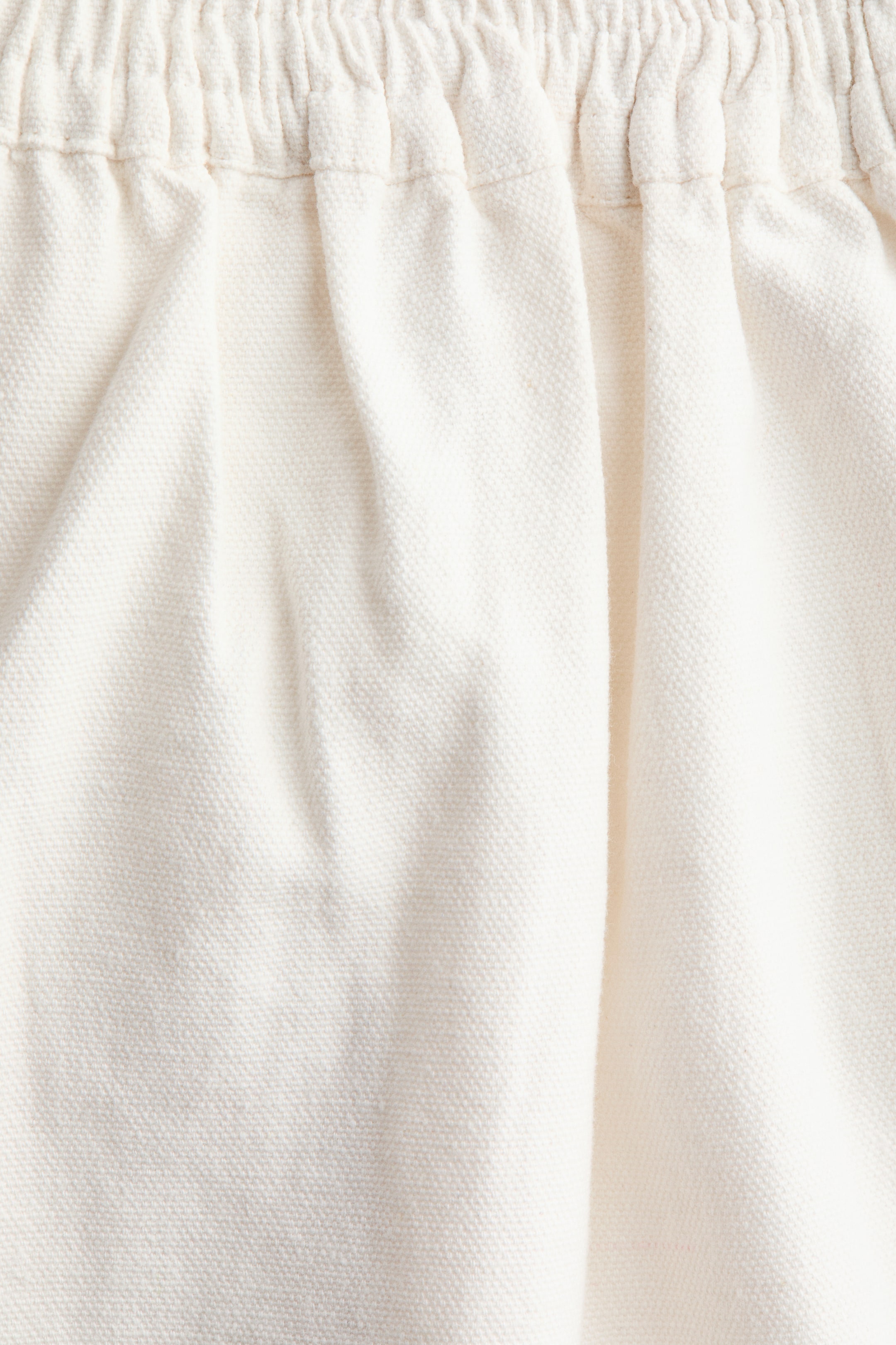 Visualizza immagine più grande: Un paio di pantaloni in tela di cotone a vestibilità ampia presenta una vita regolare con elastico coperto e arricciato, con il tessuto che cade morbido sotto.