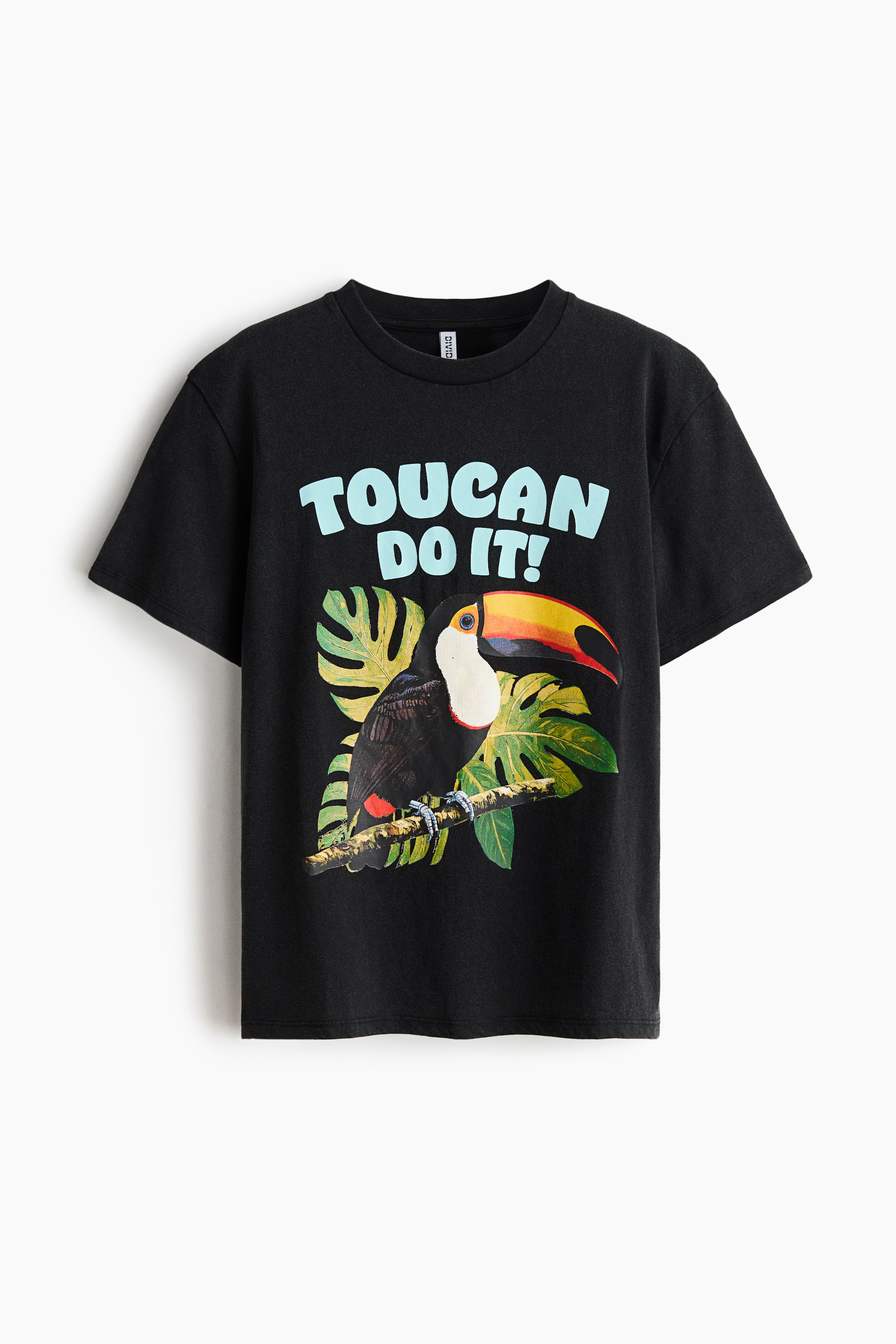 Grotere afbeelding bekijken: Het zwarte T-shirt, frontaal gepresenteerd, heeft een ronde hals en korte mouwen. Het toont een grafische print van een toekan met een kleurrijke snavel, zittend op een tak tussen groene tropische bladeren, met de lichtblauwe tekst "TOUCAN DO IT!" boven de afbeelding.