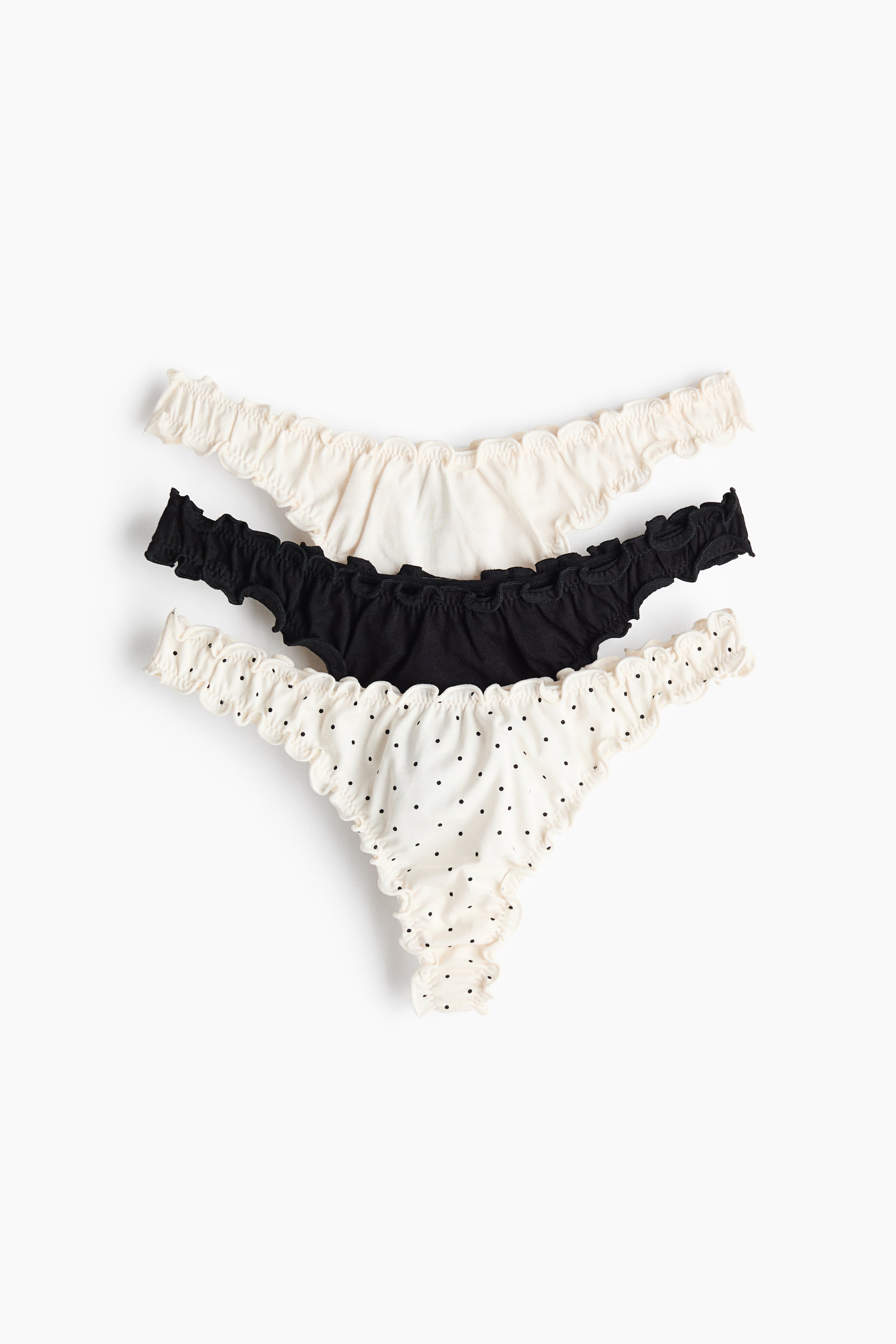 View larger image: Three thong briefs are shown from the front, each featuring ruffled overlocked edges and a low, V-shaped waistline. The set includes one off-white brief, one black brief, and one off-white brief with black polka dots.