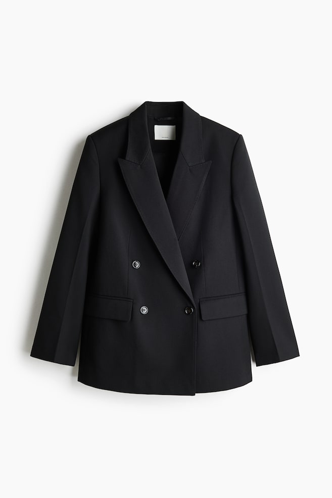 A long black double-breasted blazer is hanging front-facing, featuring wide peak lapels and a four-button fastening. The blazer showcases structured shoulders, front waist darts, and two jetted pockets with flaps. - 1