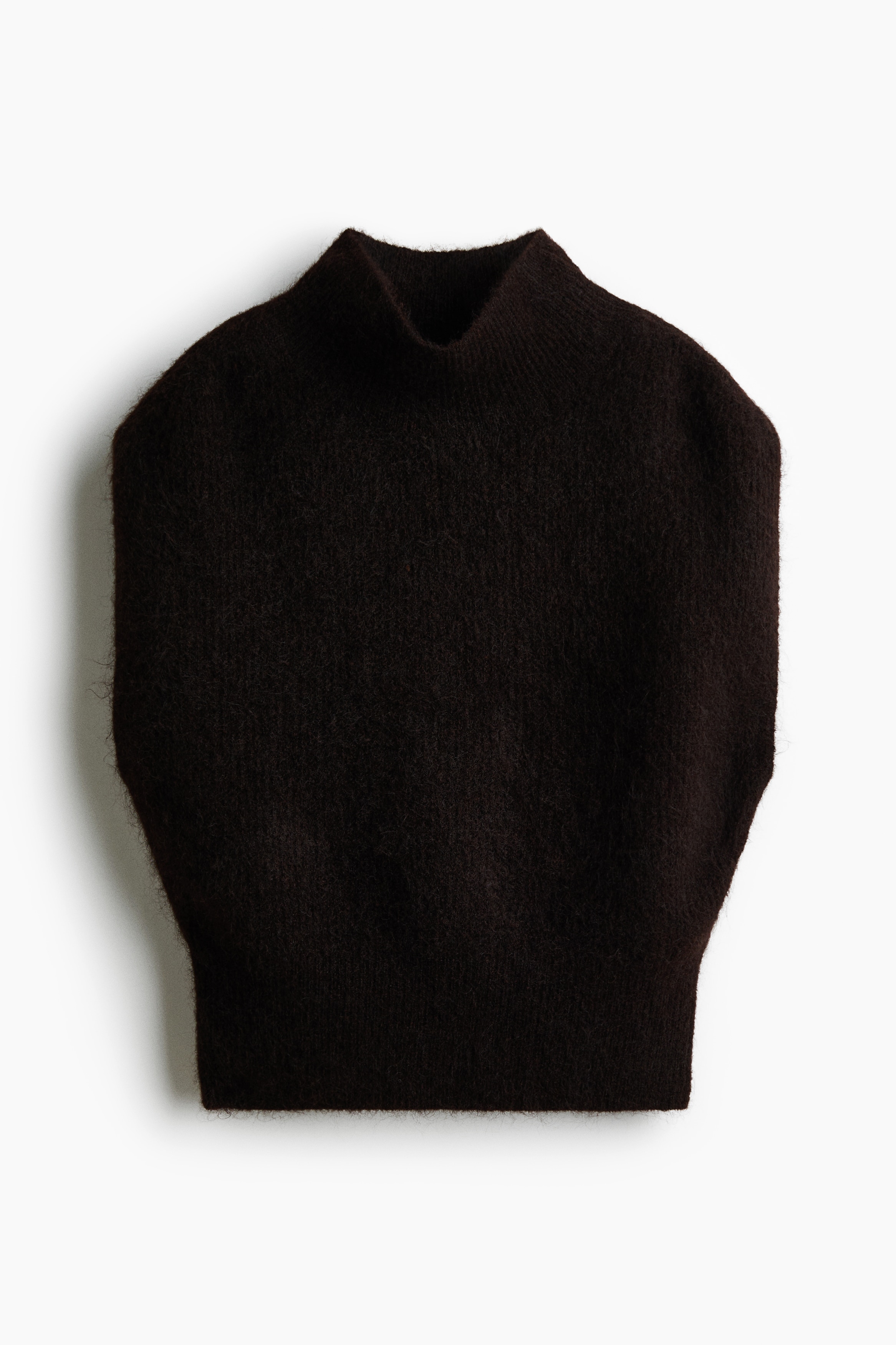 Un gilet nero dalla vestibilitÃ  ampia, in morbida maglia soffice, con collo alto e ampio bordo a costine, indossato dalla modella che tiene una mano al colletto. Il gilet senza maniche Ã¨ abbinato a jeans blu e a una giacca beige annodata in vita.