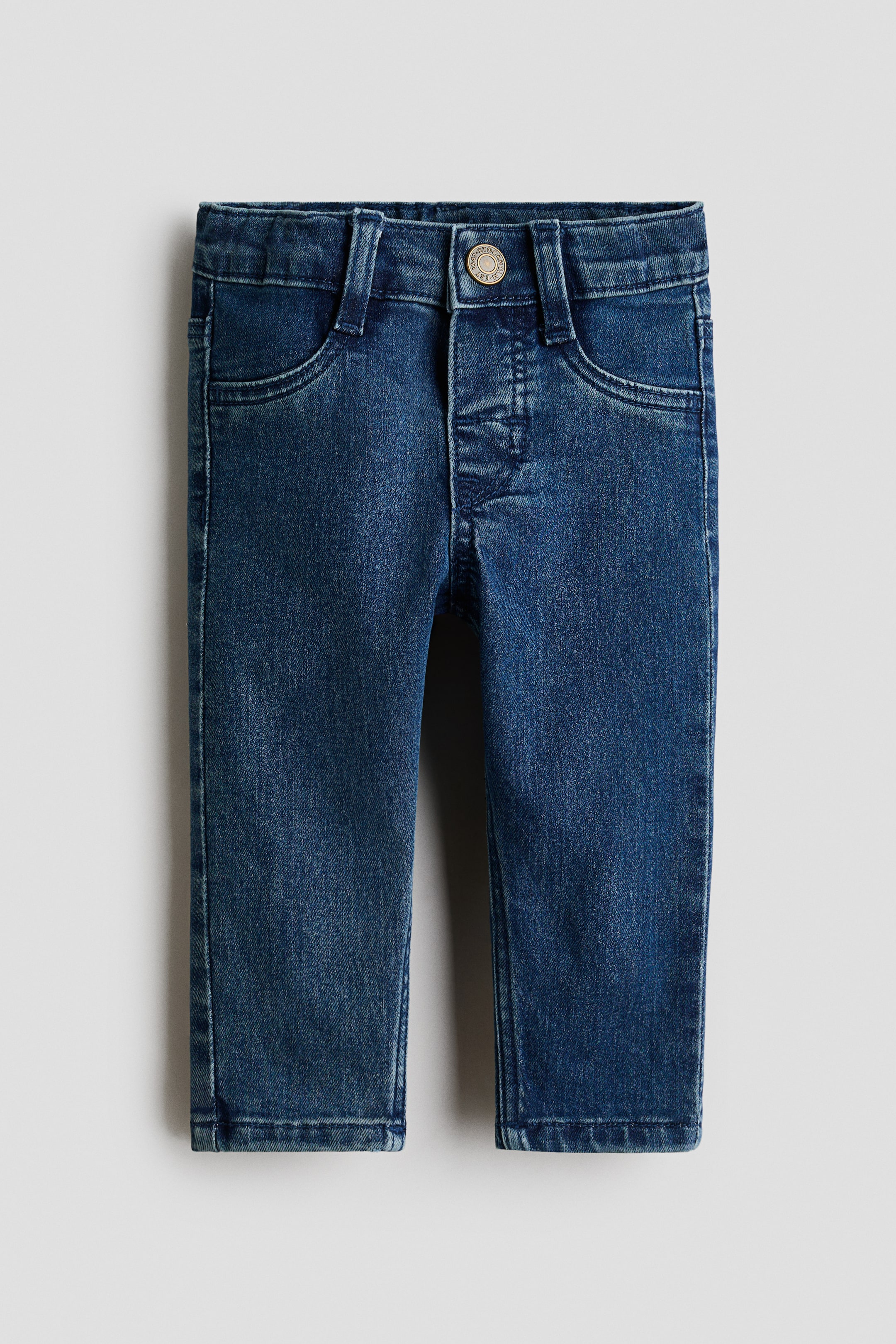 View larger image: Dark blue denim jeans are showcased from the front, highlighting a slim fit. They feature a waistband with belt loops and a single metal snap button. A faux fly with decorative stitching and two ornamental front pockets are visible.
