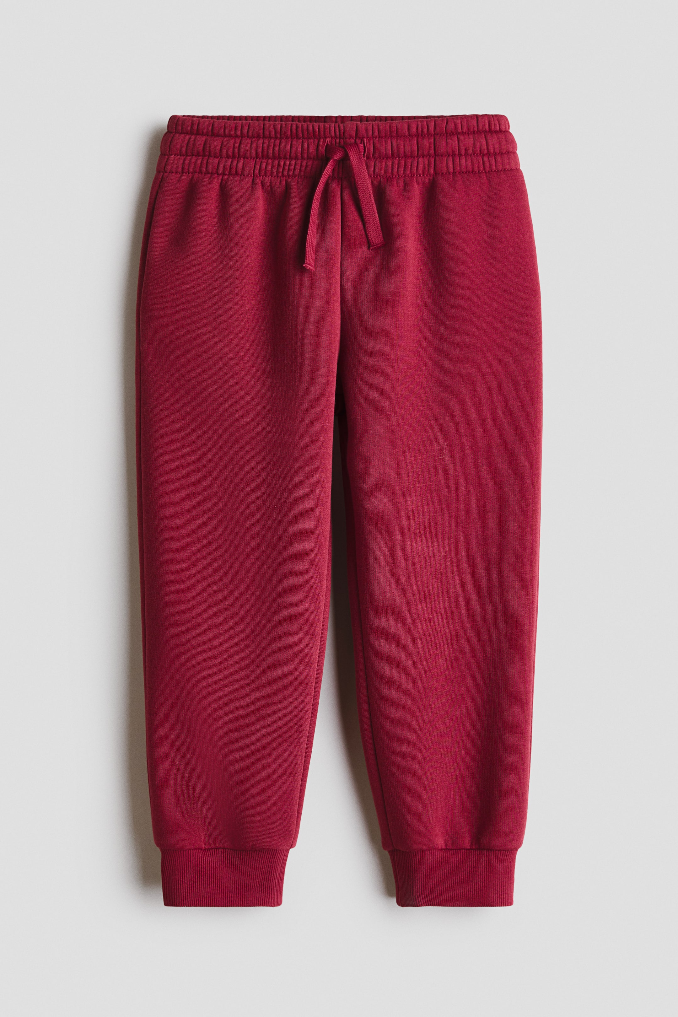 View larger image: Dark red joggers crafted from sweatshirt fabric, featuring an elasticated drawstring waist, discreet side pockets, and ribbed cuffs.