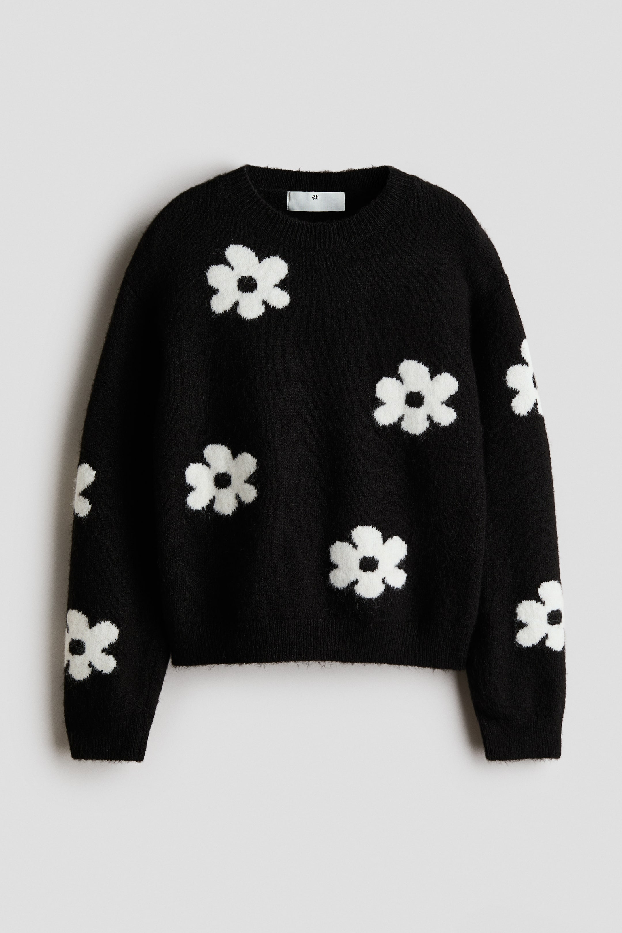 View larger image: A black jumper is showcasing its front, adorned with white daisy-like flowers throughout. It is crafted with a crew neck, ribbed cuffs, and a ribbed hem.