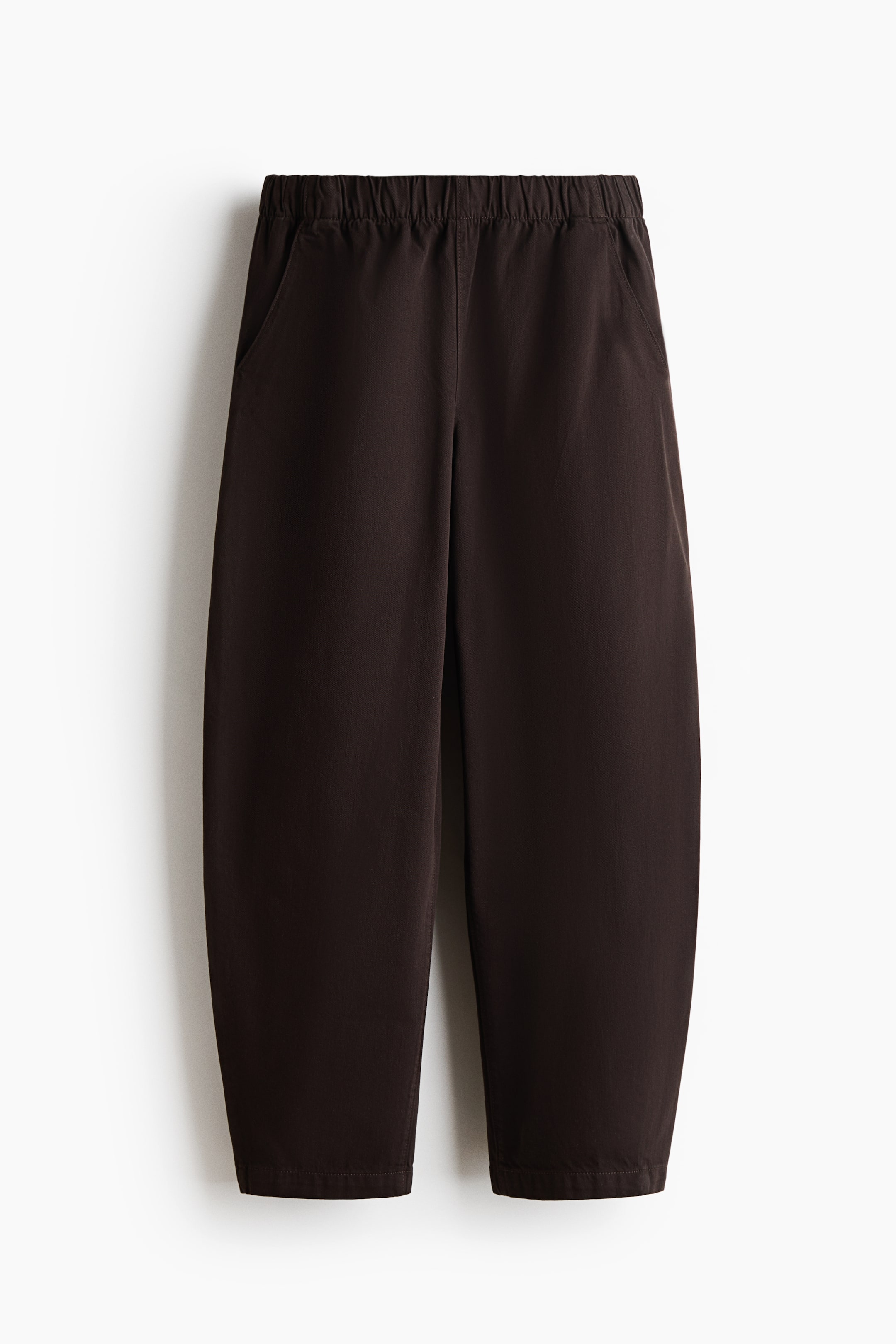 Ver imagen más grande: Pantalones marrón oscuro presentando una vista frontal, con una cintura elástica con frunces y dos bolsillos laterales inclinados. Las piernas muestran un ajuste relajado de corte barril, estrechándose ligeramente hacia dobladillos rectos y acabados.