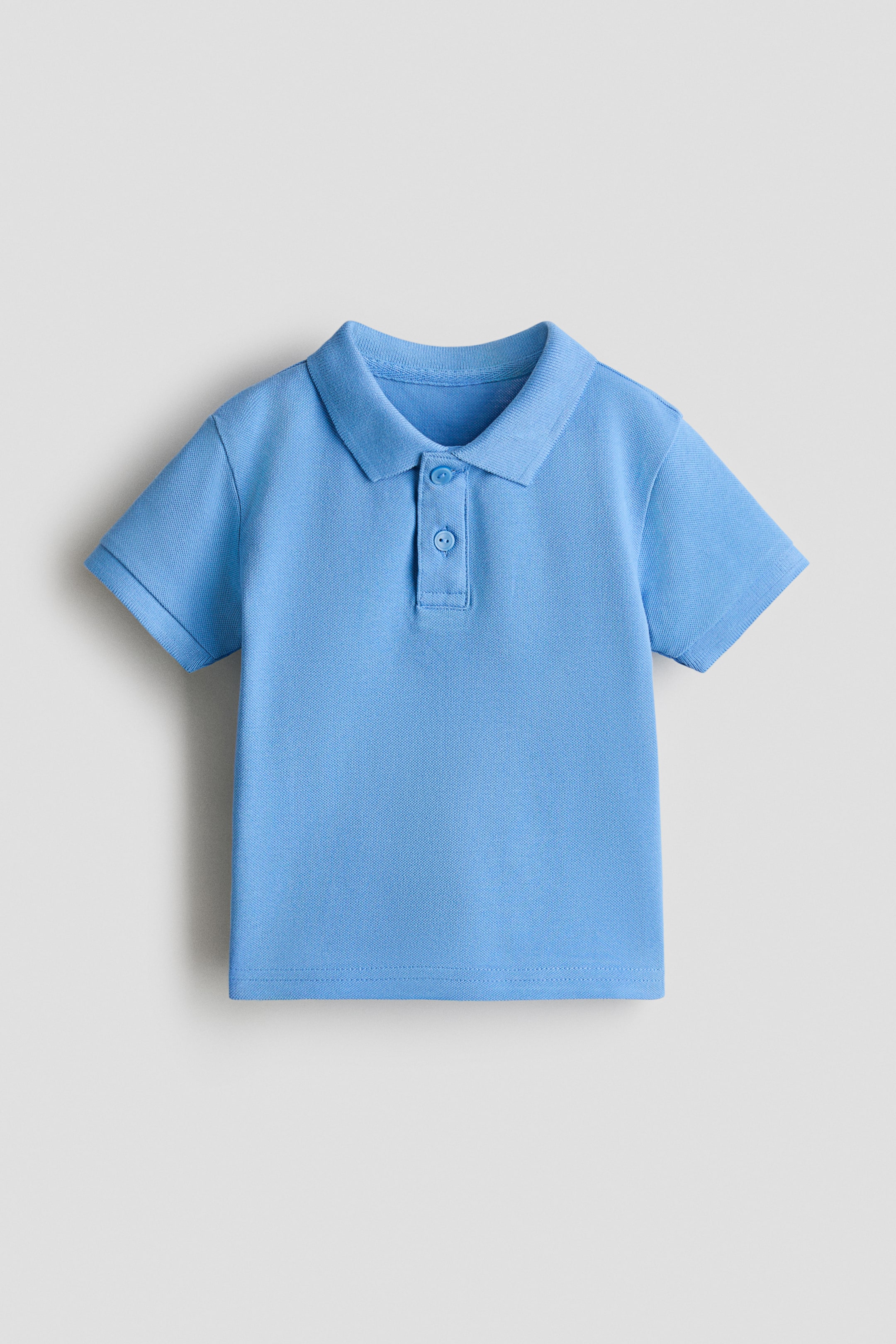 View larger image: A light blue pique knit polo shirt is facing front, featuring a classic collar, a two-button placket with light-coloured buttons, and short cuffed sleeves.
