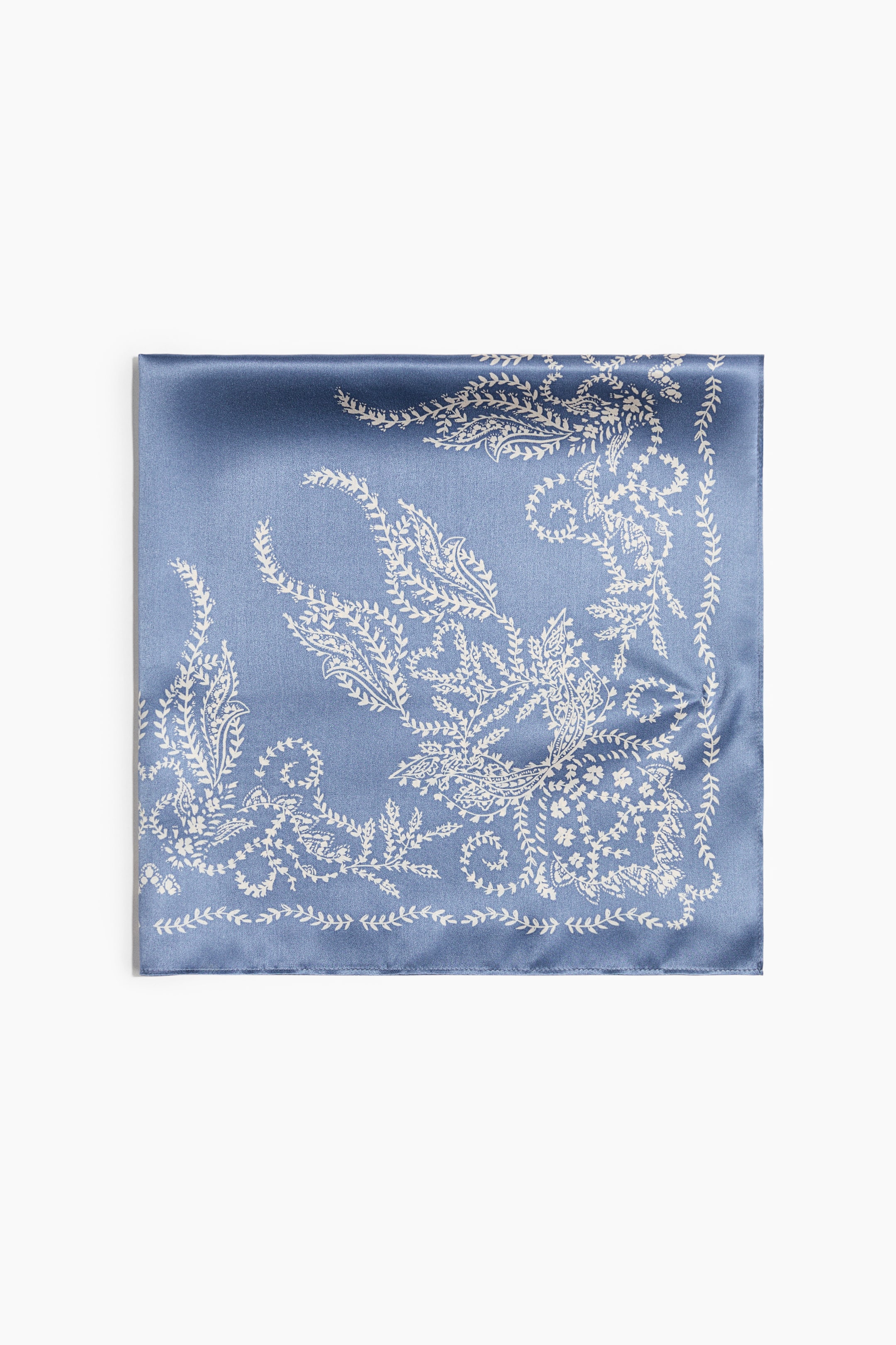 View larger image: A square silk scarf in dusty blue is laid flat, front-facing, showcasing a white botanical and paisley print concentrated along the borders and corners. The scarf features a smooth, satin-like finish with stitched edges.