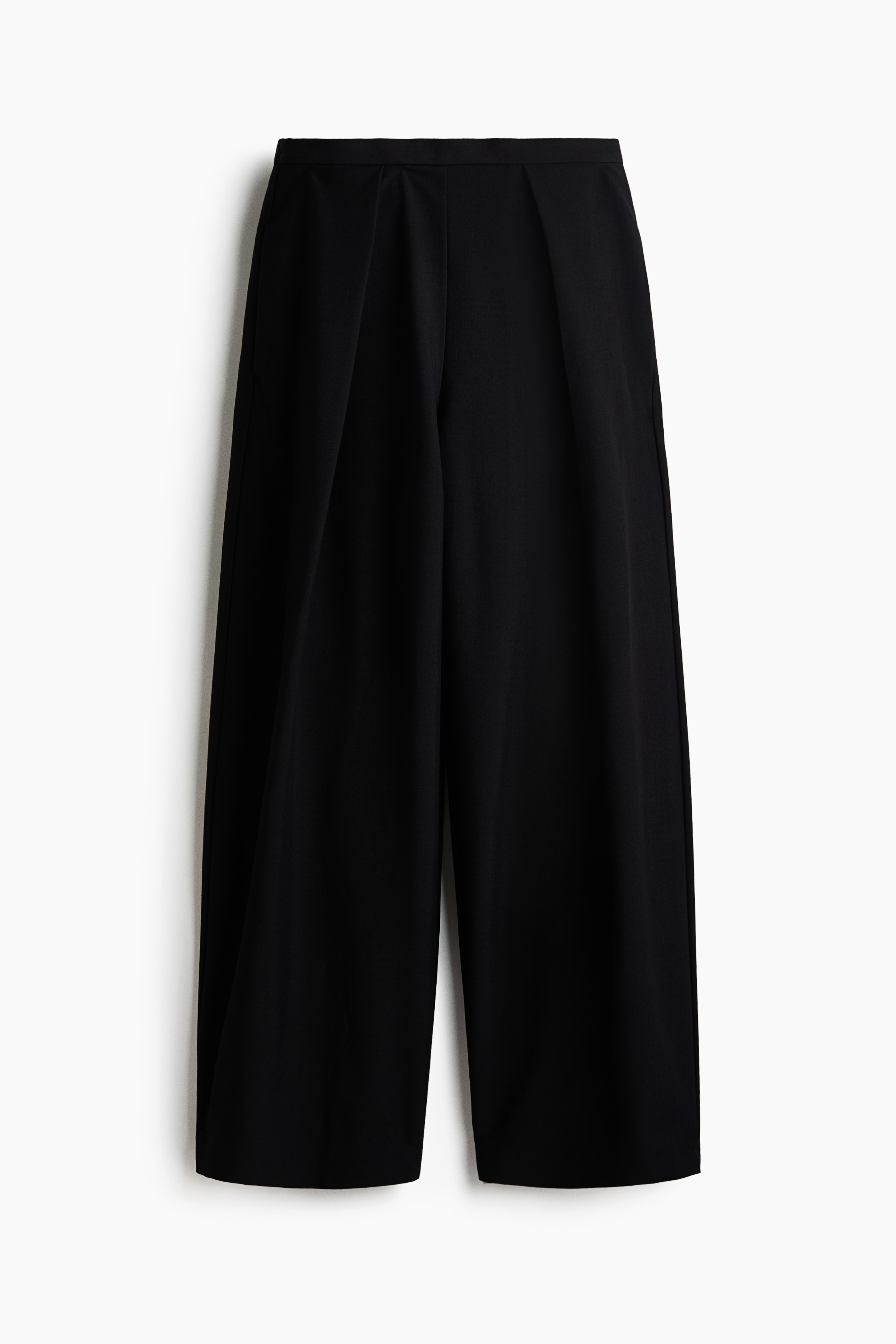Sorte løstsiddende bukser i satin twill bæres af modellen, som sidder med hænderne hvilende i sidelommerne. De vide bukser har en normal talje og er stylet med en mørk crop top, en jakke med leopardprint og sneakers i neutrale farver.