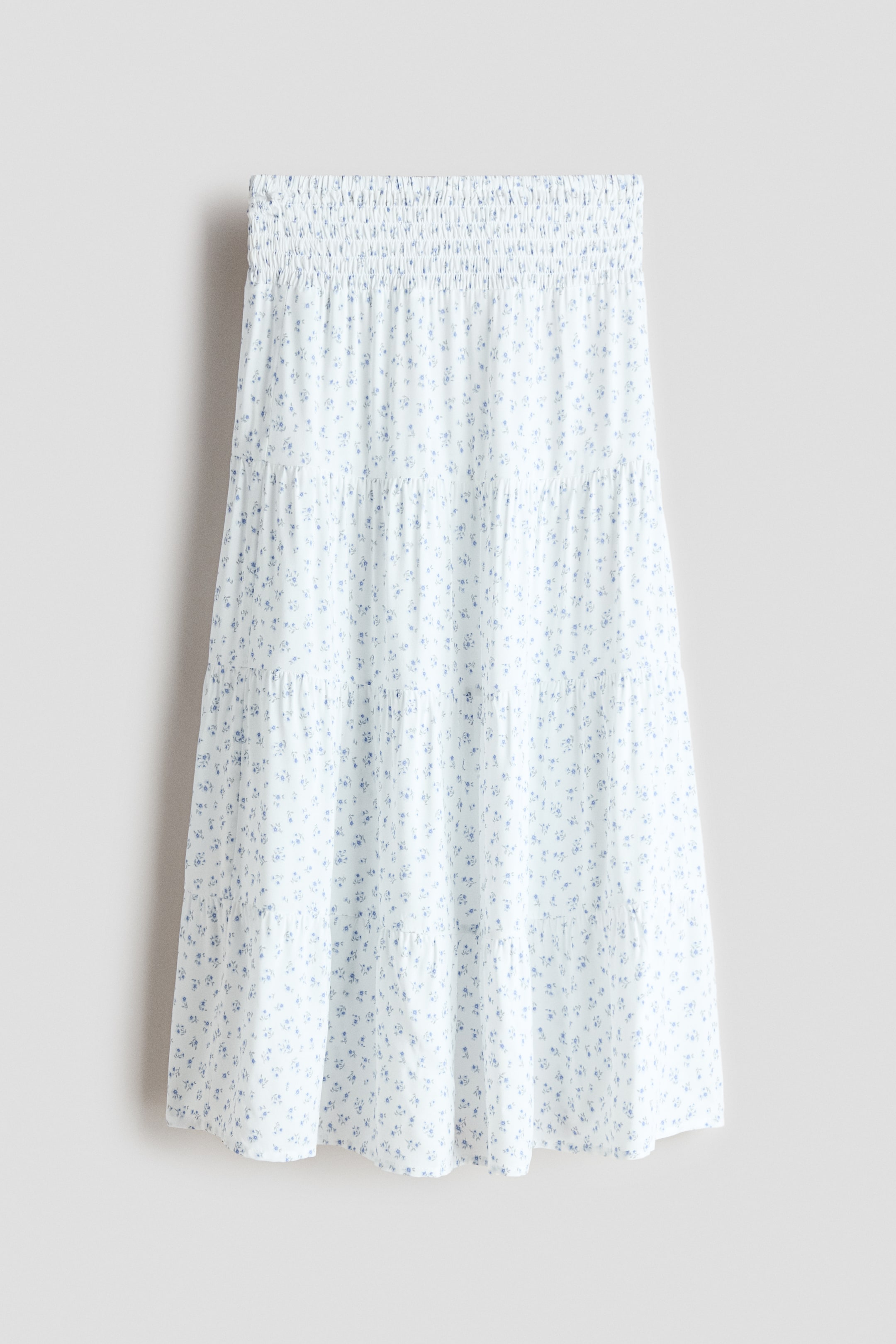 View larger image: The front-facing skirt showcases a white fabric adorned with a delicate blue floral print, featuring a shirred waistband and a tiered design.