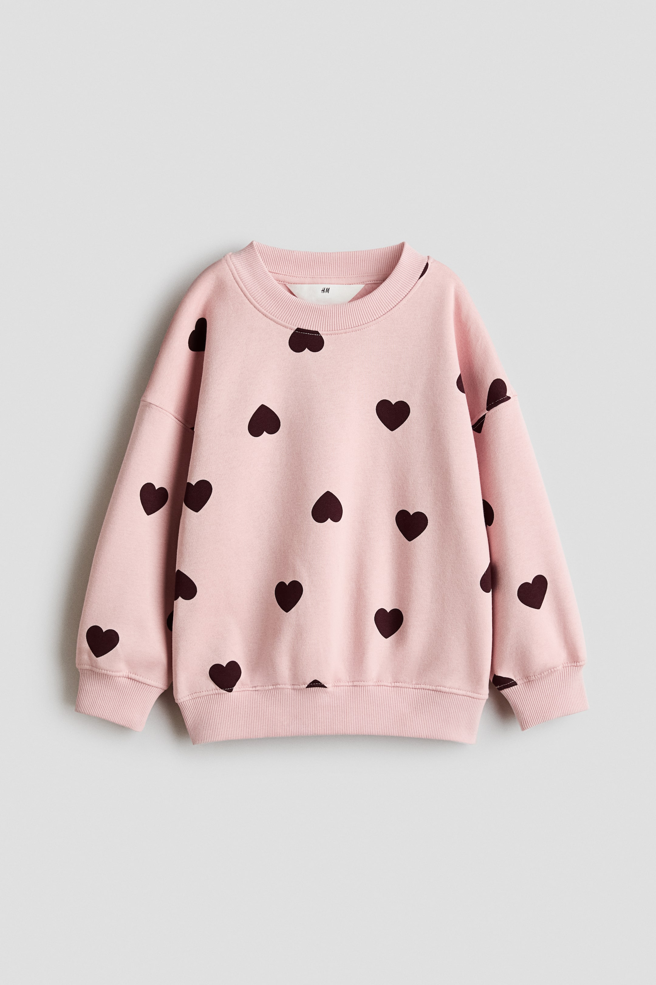 View larger image: An oversized pink sweatshirt shown from the front. It features dark heart patterns all over, a round ribbed neckline, dropped shoulders, long sleeves, and ribbed cuffs and hem.