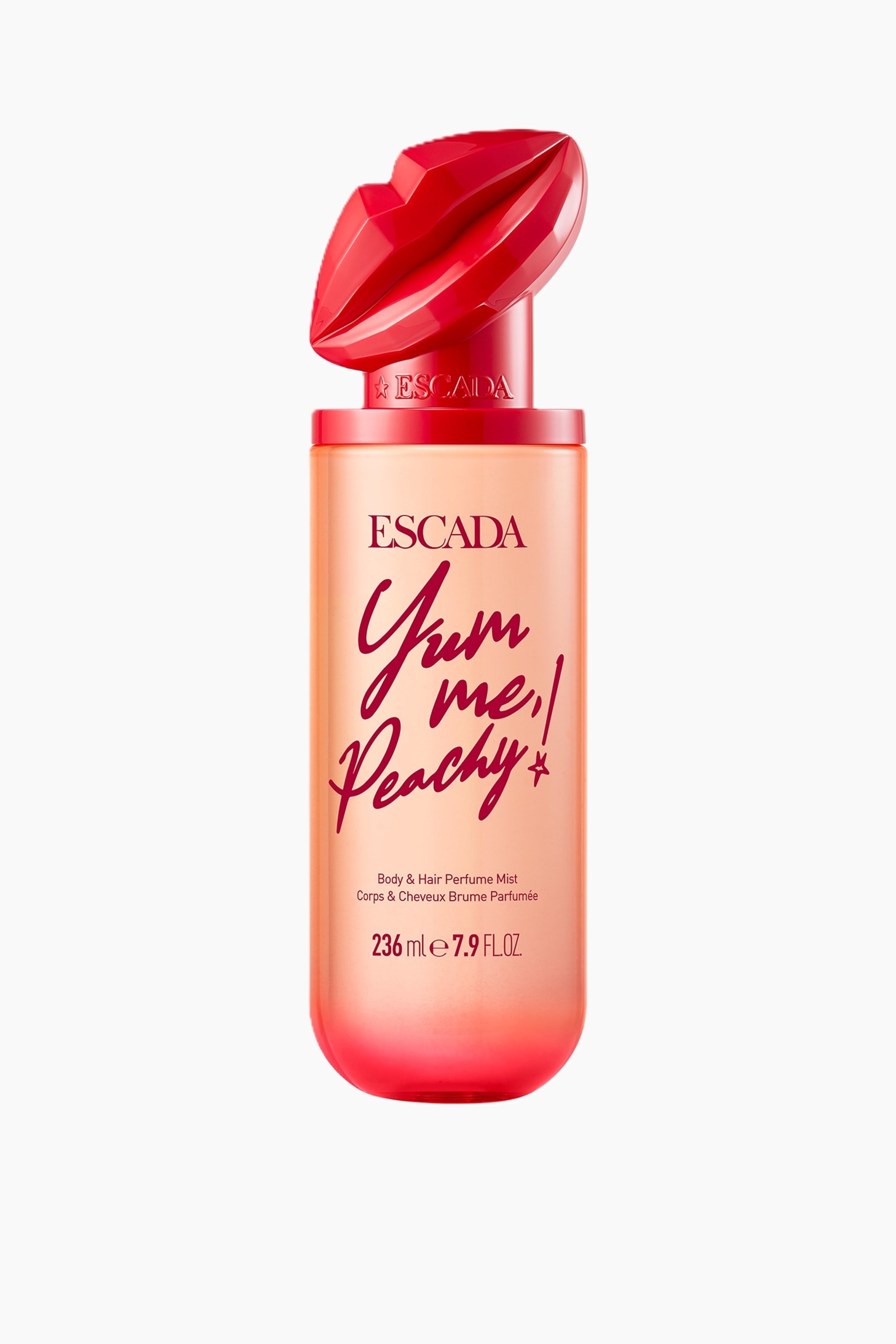 Se større billede: En Escada krops- og hårparfume-mistflaske står oprejst og har en klar cylindrisk krop med en ombre-effekt, der går fra ferskenorange til levende pink-rød. Den er toppet med en facetslebet rød læbeformet hætte, og "Yum me! Peachy!" vises i rød skrift på forsiden.