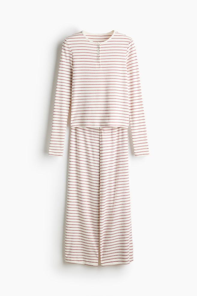 A two-piece lounge set is hanging in a front view, featuring a long-sleeved henley top and matching wide-leg pants. Both pieces are displaying an off-white ribbed fabric patterned with thin, horizontal red stripes, with the top including a short button placket at the neckline. - 1