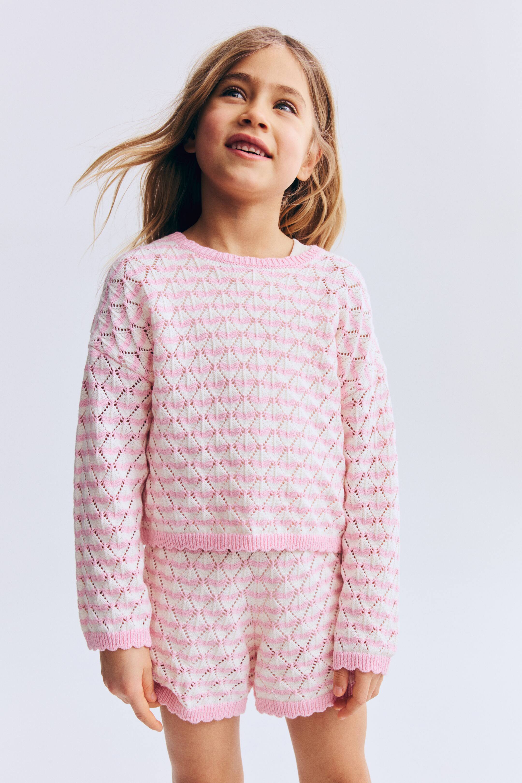 View larger image: A pink-and-white two-piece knit set features a diamond-shaped openwork pattern throughout. The long-sleeved top has a crew neck, ribbed cuffs and a ribbed hem, while the matching shorts have a ribbed, scalloped hem.