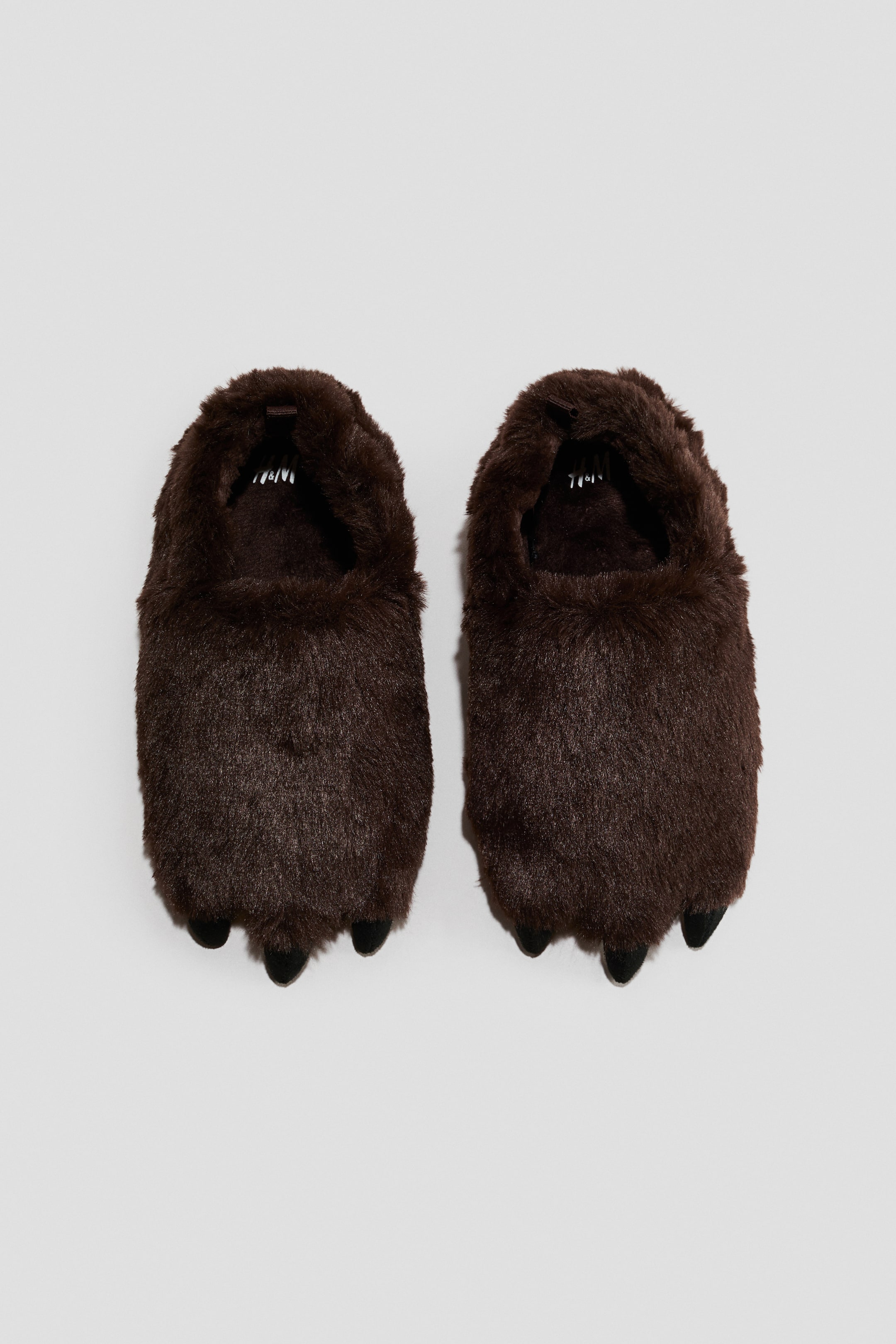 Voir une image plus grande: Une paire de pantoufles en fausse fourrure hirsute brun foncé est placée côte à côte, orientée vers l’avant, chacune présentant un design en forme de patte avec trois protubérances noires semblables à des griffes à l’avant-pied.