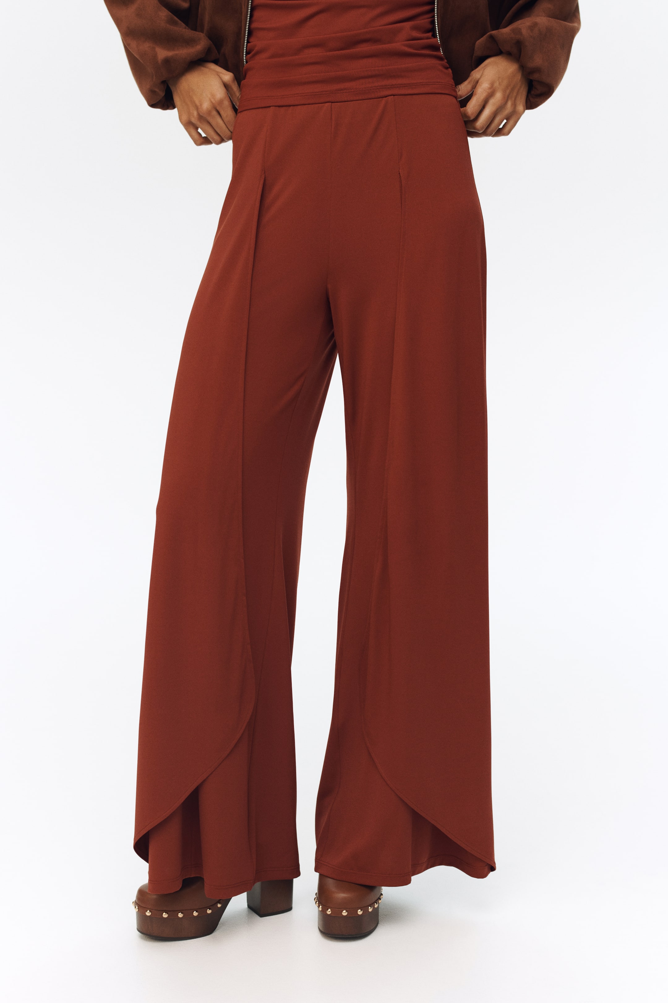 Ver imagem maior: Calças de perna larga em tom ferrugem apresentam uma cintura alta e franzida, costuras verticais na frente e uma bainha sobreposta em forma de tulipa.