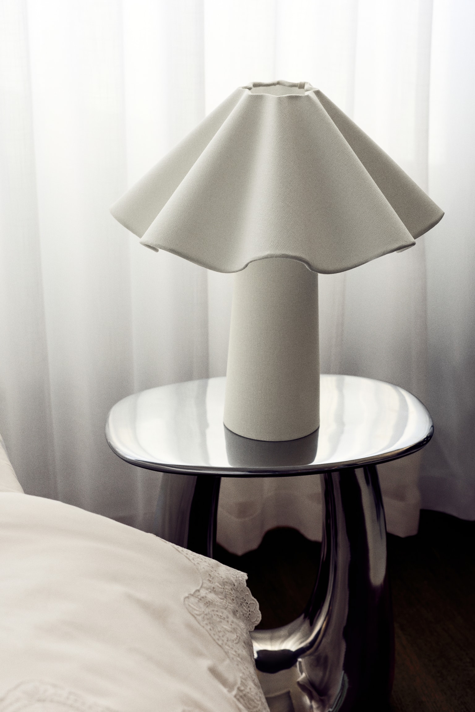 En bordlampe med en konisk base og en flæseformet, klokkeformet skærm, begge med en off-white, tekstureret finish, samt en grå flettet strømkabel, der strækker sig fra basen. - 1