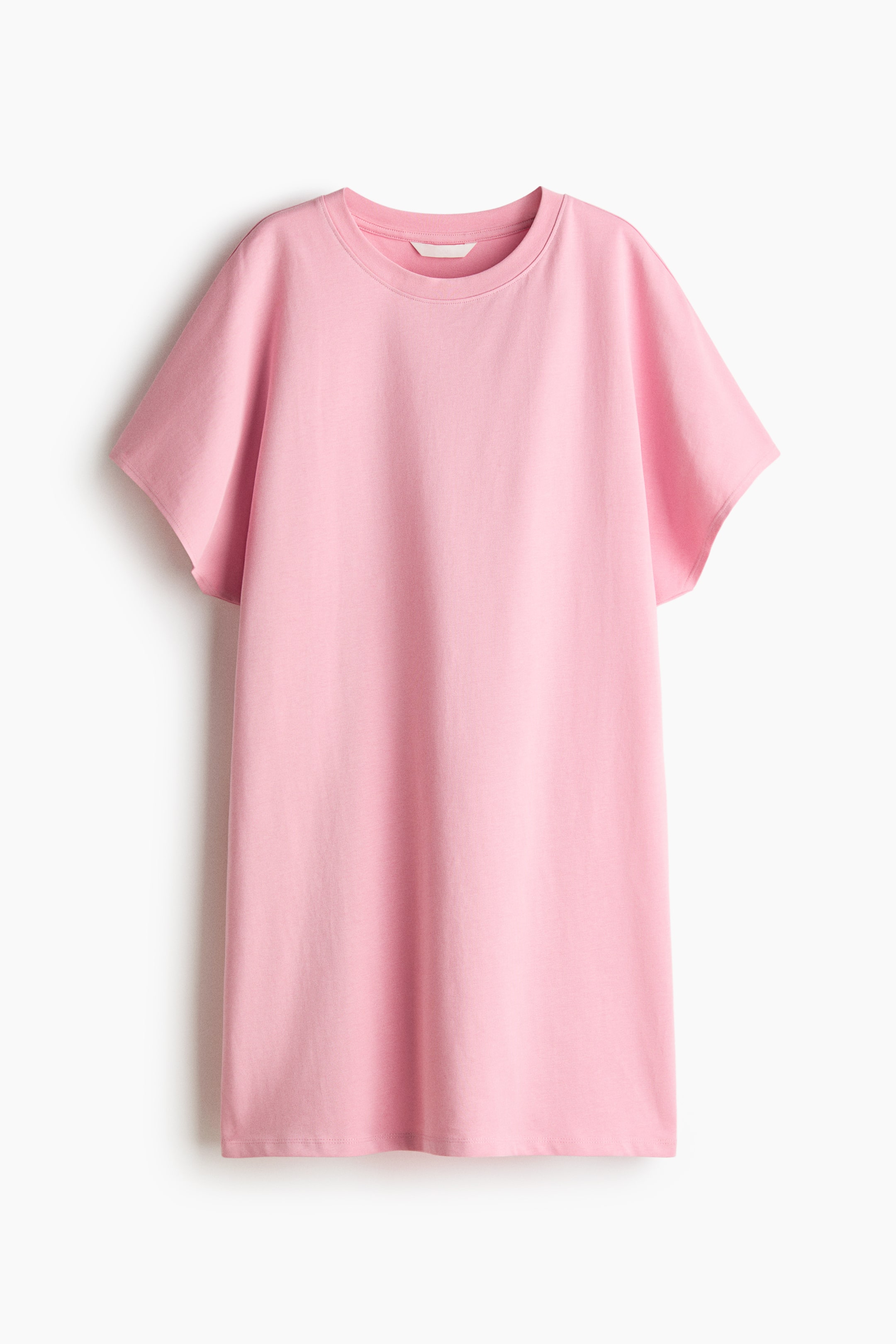 View larger image: The pink t-shirt is shown from the front, featuring a round ribbed neckline and short, loose sleeves. A small white tag is visible inside the back of the neck, and the longer-length shirt displays a straight hem.
