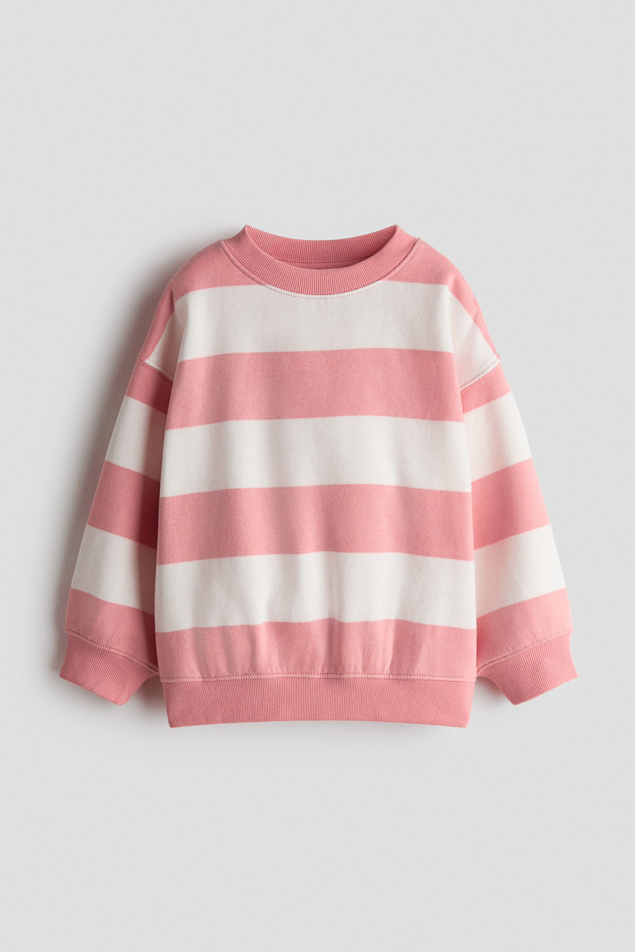 View larger image: A striped top is shown from the front, featuring alternating pink and white horizontal bands, a ribbed crew neckline, dropped shoulders, long sleeves, and ribbed cuffs and hem.