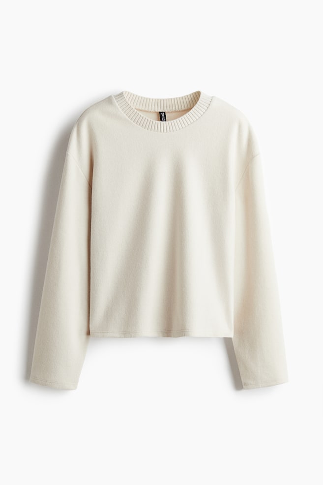 An off-white, short, oversized sweatshirt in jersey with a soft brushed finish is being shown from the FRONT, featuring a round, rib-trimmed neckline, dropped shoulders, and long sleeves. - 1