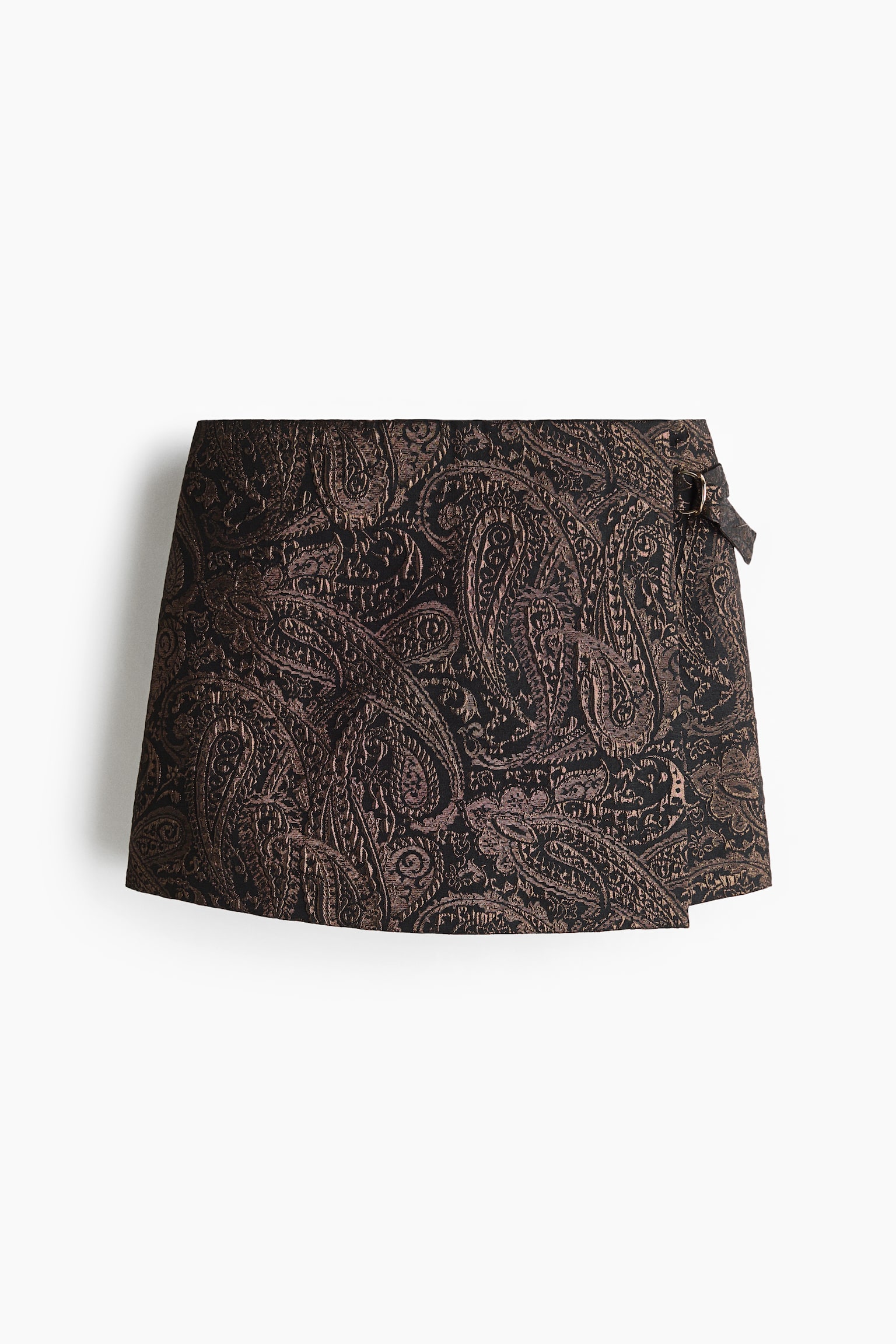 A wrap miniskirt, front-facing, features a textured metallic bronze and black paisley jacquard pattern. The skirt showcases an asymmetrical wrap design with a small metal buckle fastening at the side waist.