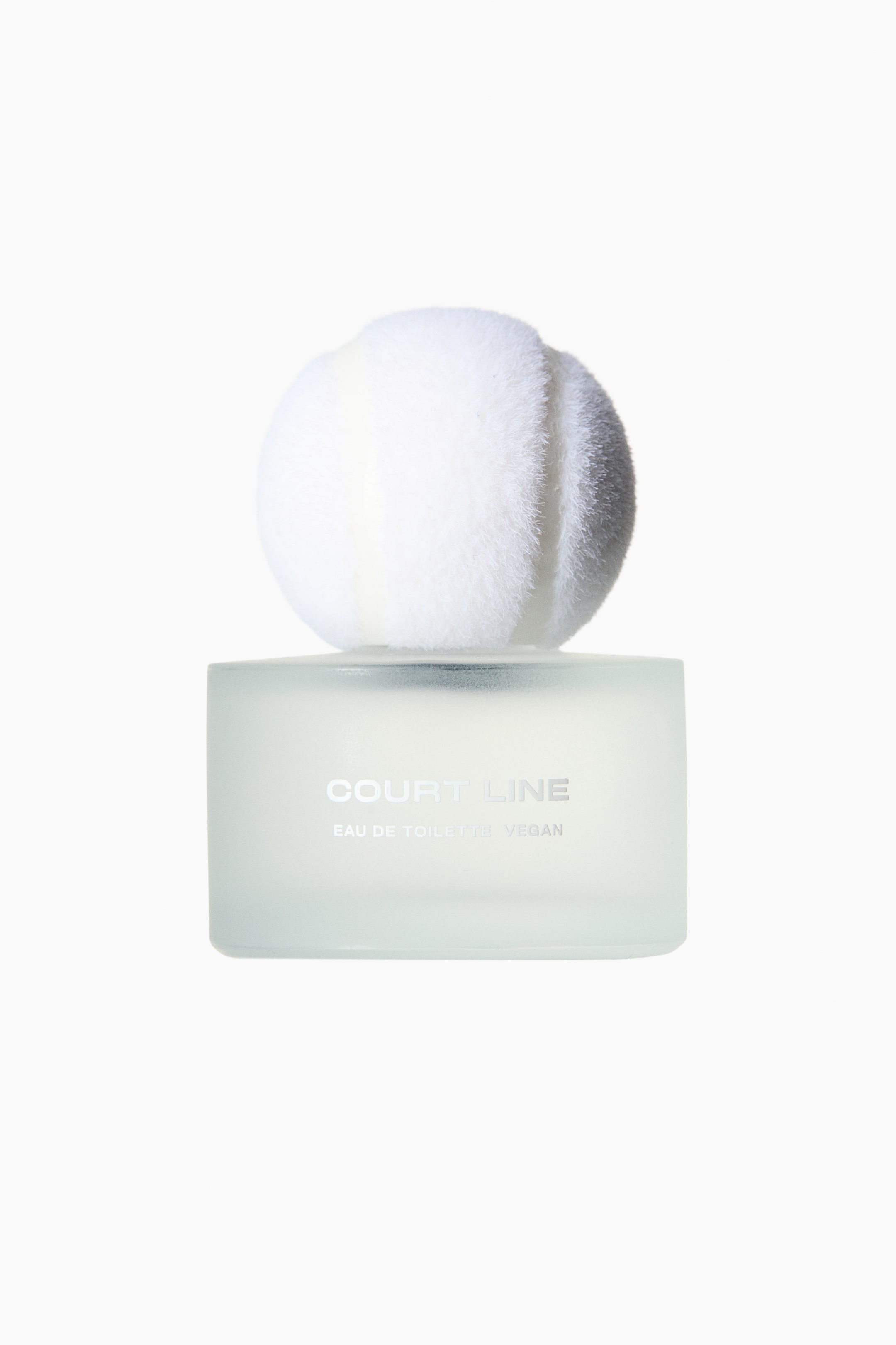 View larger image: Court Line EdT showcases a front view of its translucent, frosted glass bottle, prominently displaying "COURT LINE" with "EAU DE TOILETTE VEGAN" beneath it. A large, fluffy white and grey spherical cap tops the bottle.