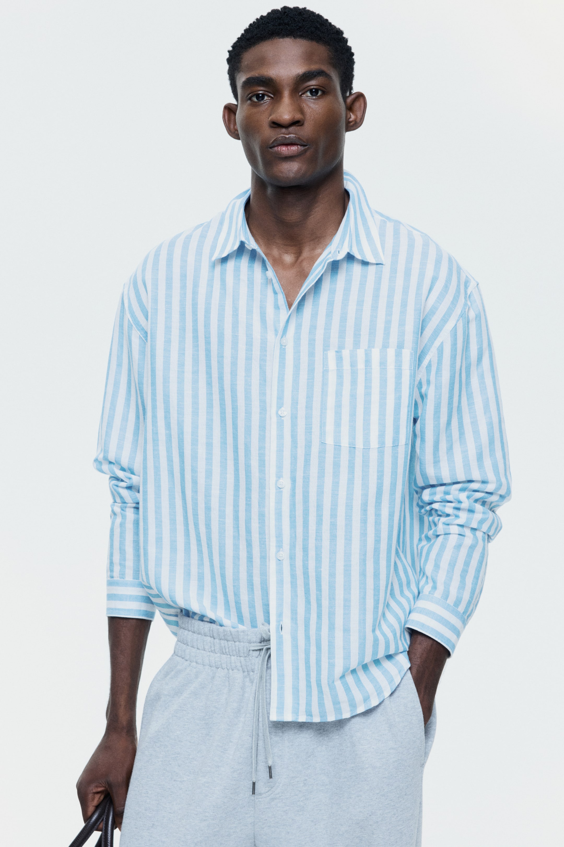 View larger image: A light blue and white striped long-sleeved shirt featuring a spread collar, a button-front closure, and a patch pocket on the left chest. The shirt presents a relaxed, untucked fit with buttoned cuffs and is viewed from the front.