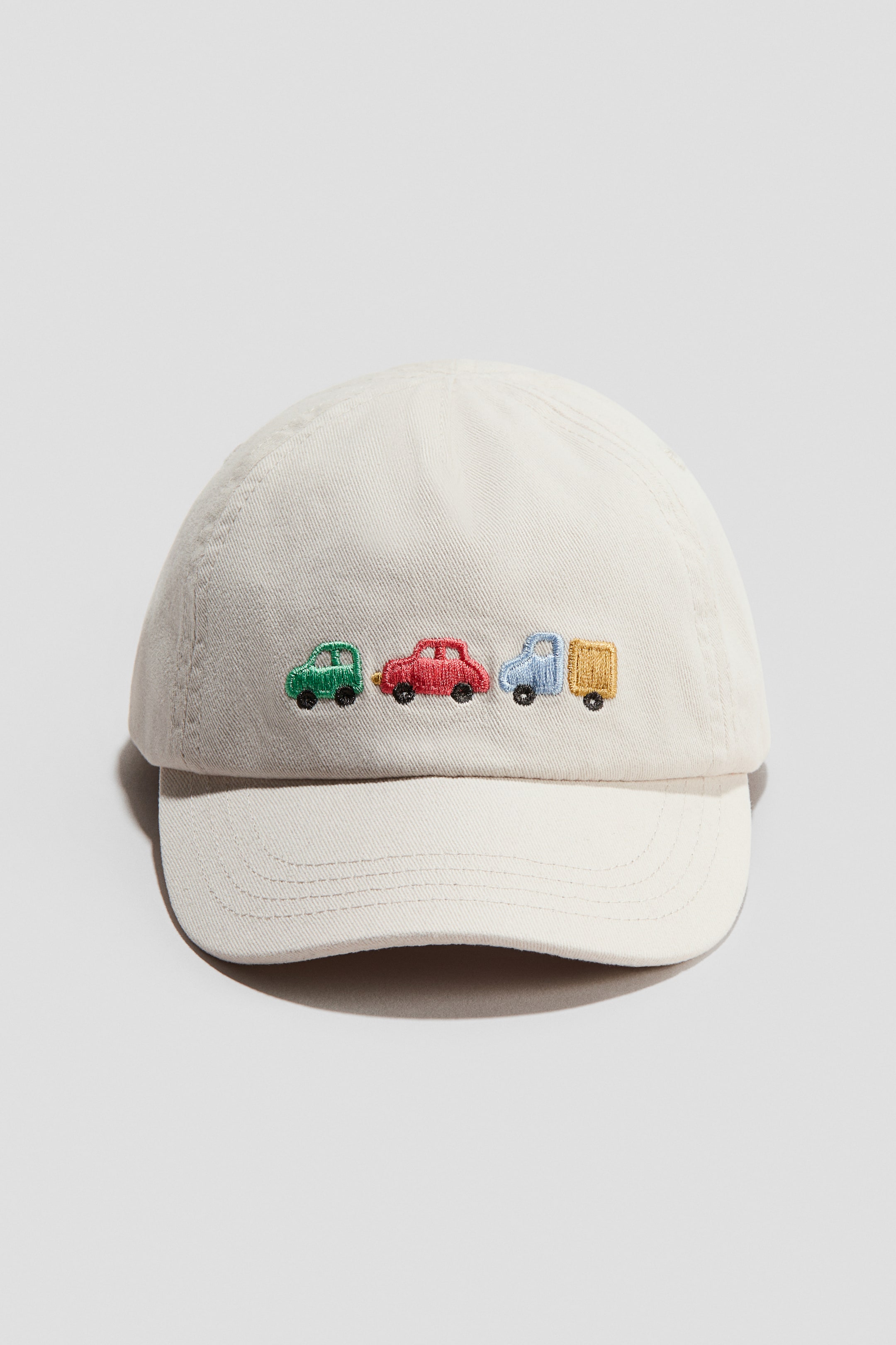 View larger image: This cap showcases its FRONT, meticulously crafted from an off-white cotton weave fabric. The front panel features a vibrant array of embroidered vehicles, including a green car, a red car, a blue truck, and a yellow truck with a trailer.