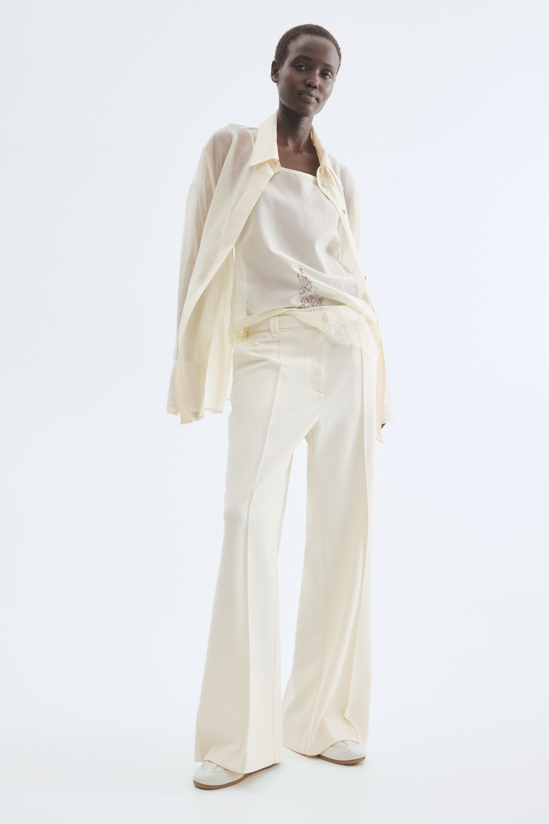 View larger image: A light cream ensemble is showcased directly, featuring a sheer long-sleeved blouse worn open over a square-neck camisole with a lace-trimmed hem. The camisole is tucked into high-waisted, wide-leg trousers with a visible front crease.