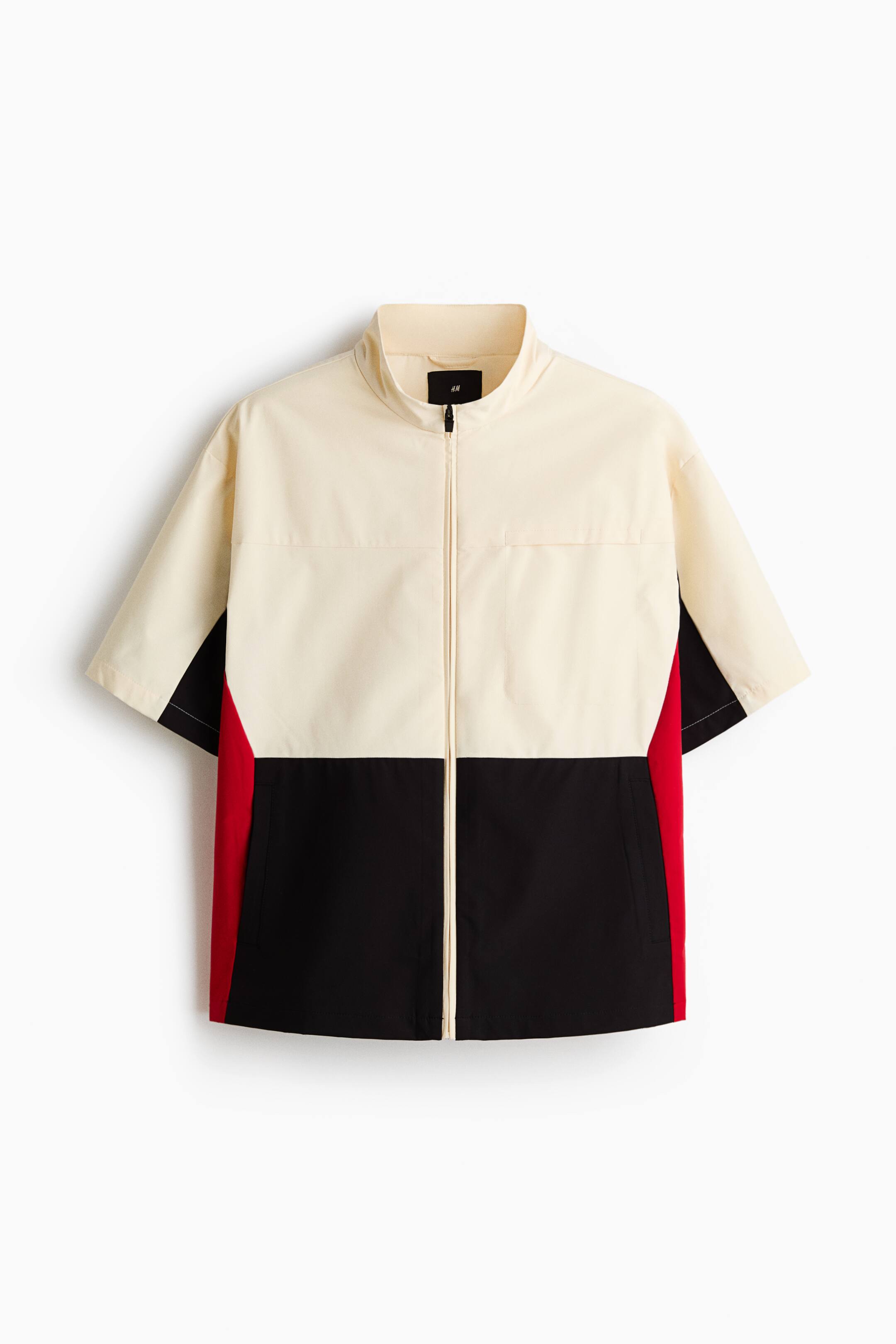 View larger image: A short-sleeved jacket is featuring a color-blocked design in cream, black, and red, presenting its FRONT with a stand-up collar and a full-length front zipper.