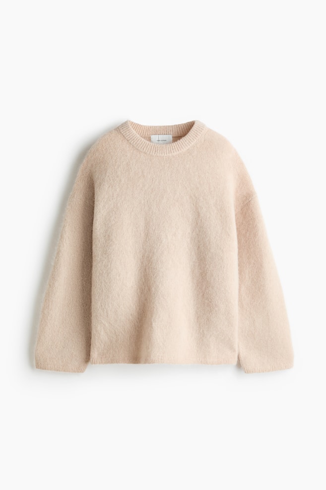 An oversized light beige jumper is displayed from the front, featuring a soft, fuzzy knit texture. It is designed with dropped shoulders, long sleeves, and a ribbed round neckline, cuffs, and hem. - 1