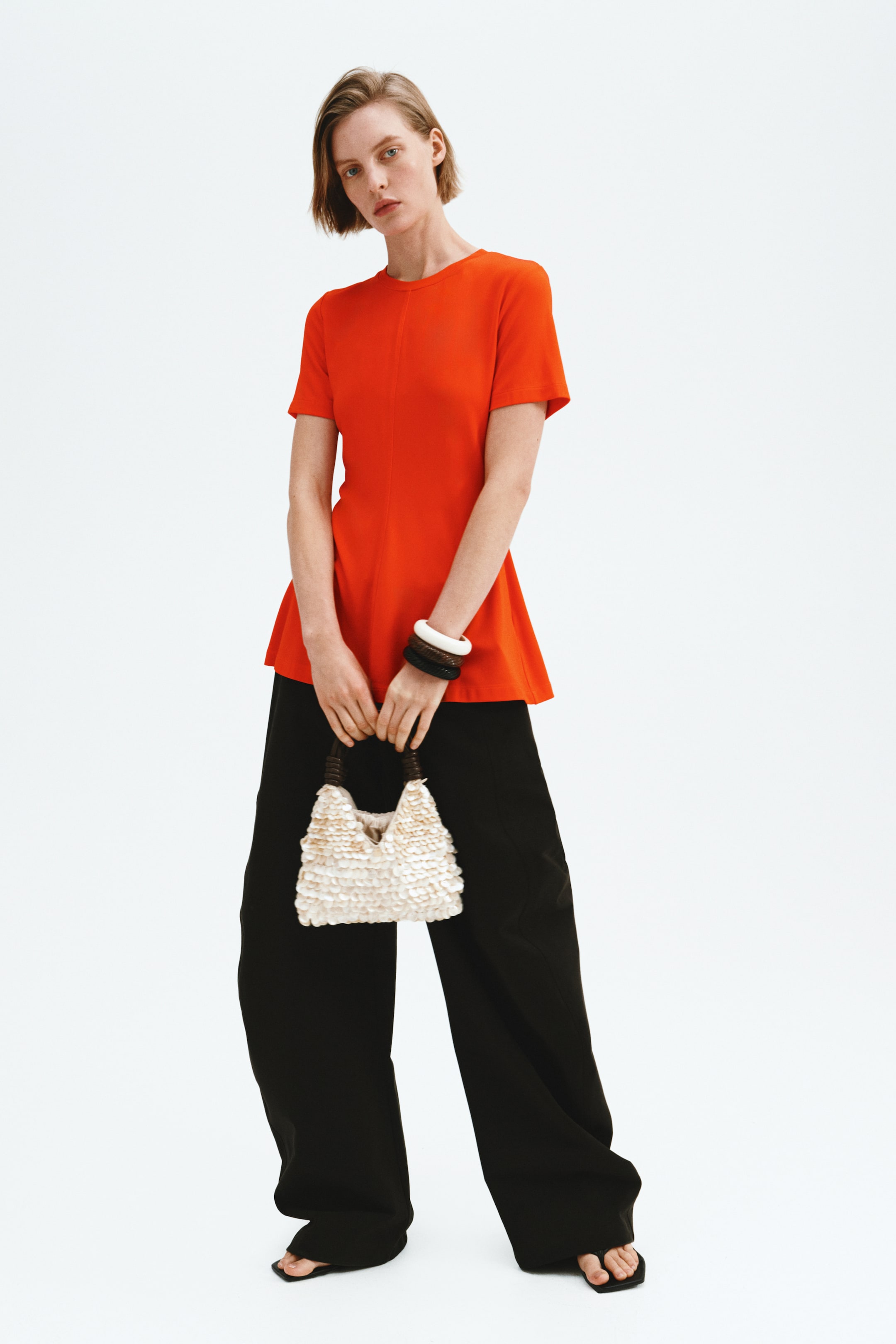 Ver imagem maior: O top vermelho apresenta uma gola redonda, mangas curtas e uma costura central vertical à frente. É desenhado com uma silhueta em linha A, alargando a partir da cintura até ao comprimento de túnica.