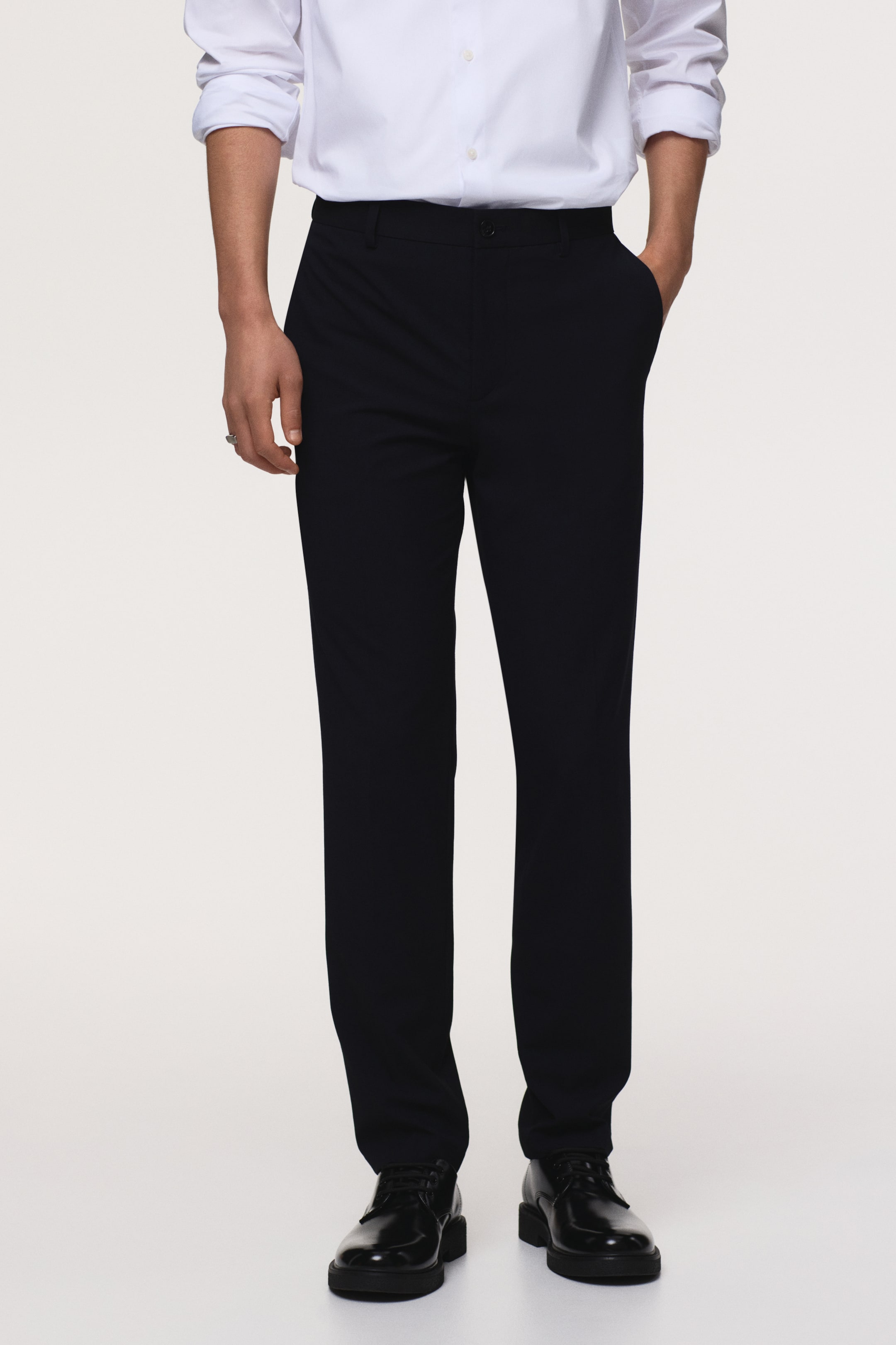 Agrandir l'image: Pantalons noirs affichant une coupe droite avec un design à devant plat et une fermeture à bouton unique à la taille. Les poches latérales sont visibles, avec une main reposant nonchalamment dans une poche, et les pantalons tombent élégamment jusqu'à la cheville.