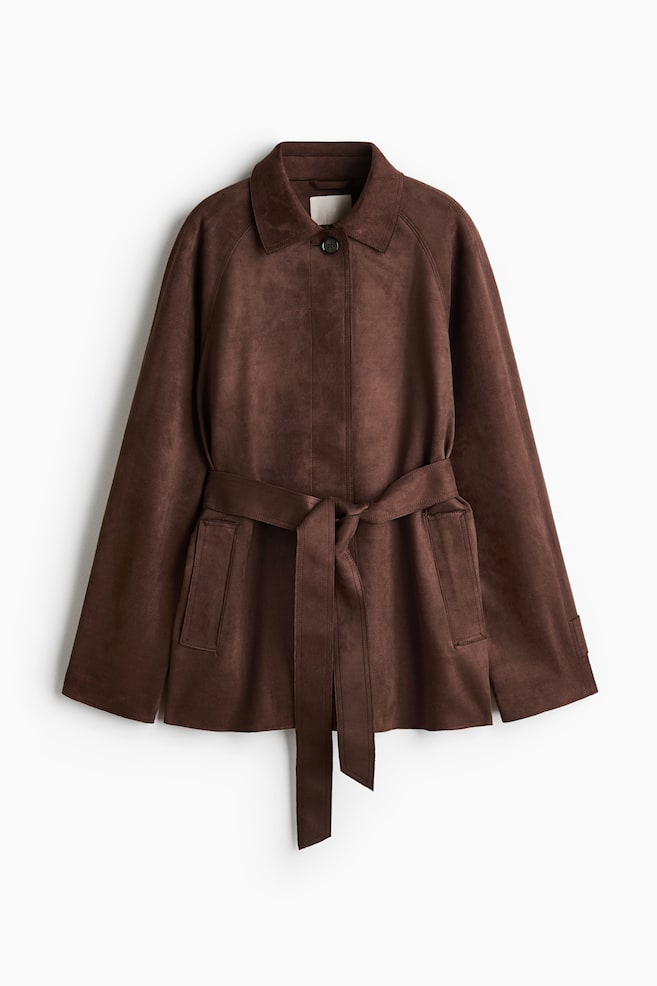 Eine braune Jacke aus Kunstwildleder mit klassischem Kragen, Raglanärmeln und einem einzelnen Knopfverschluss am Hals. Ein passender Gürtel ist um die Taille gebunden, und zwei aufgesetzte Taschen sind unterhalb des Gürtels sichtbar. - 1