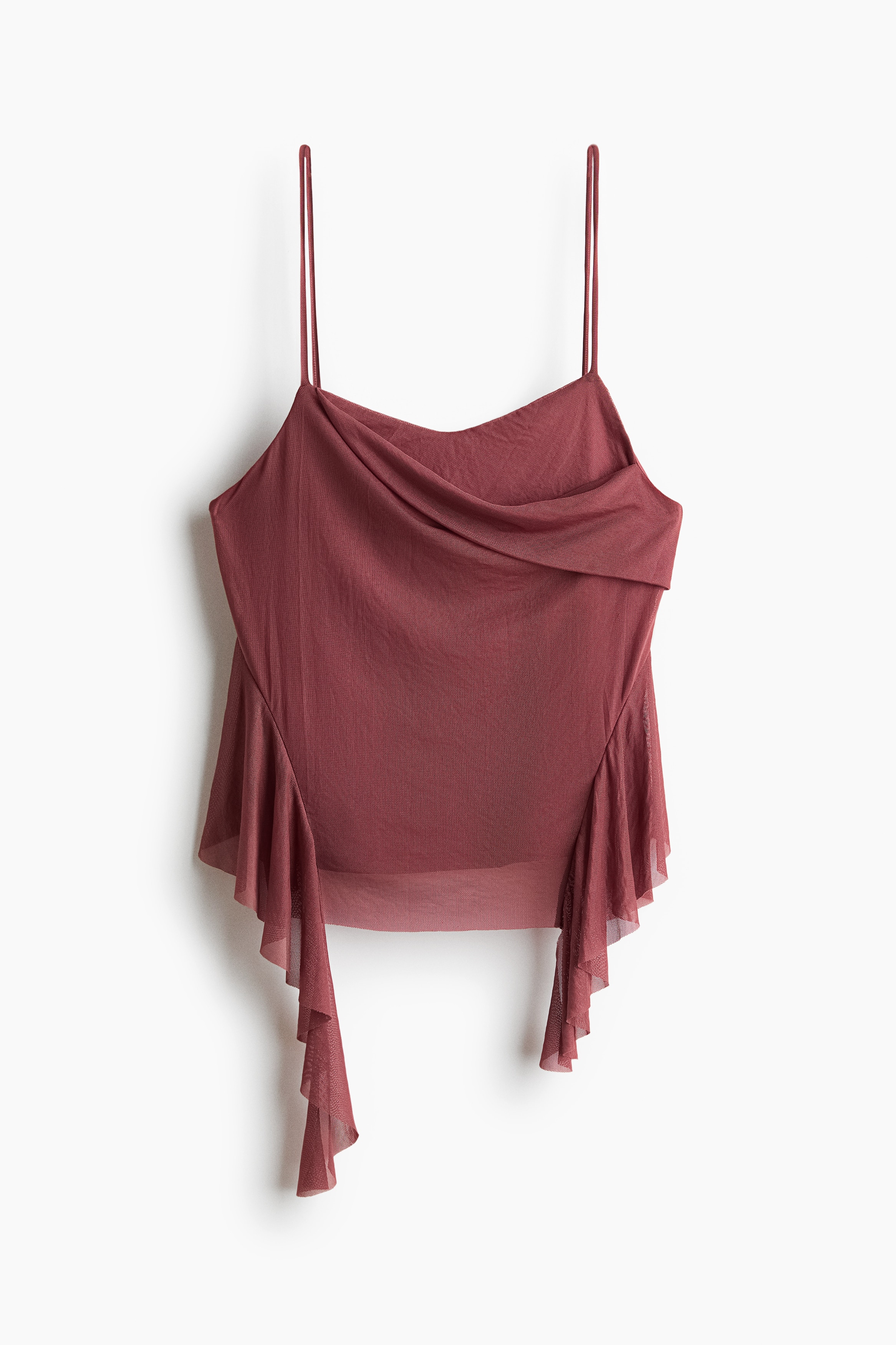 A sheer mesh cami in dark rose is being worn by the model, featuring thin spaghetti straps, an asymmetrical foldover front, and cascading flounced ruffles down the sides of an uneven hem. The top is styled with light beige wide-leg jeans.
