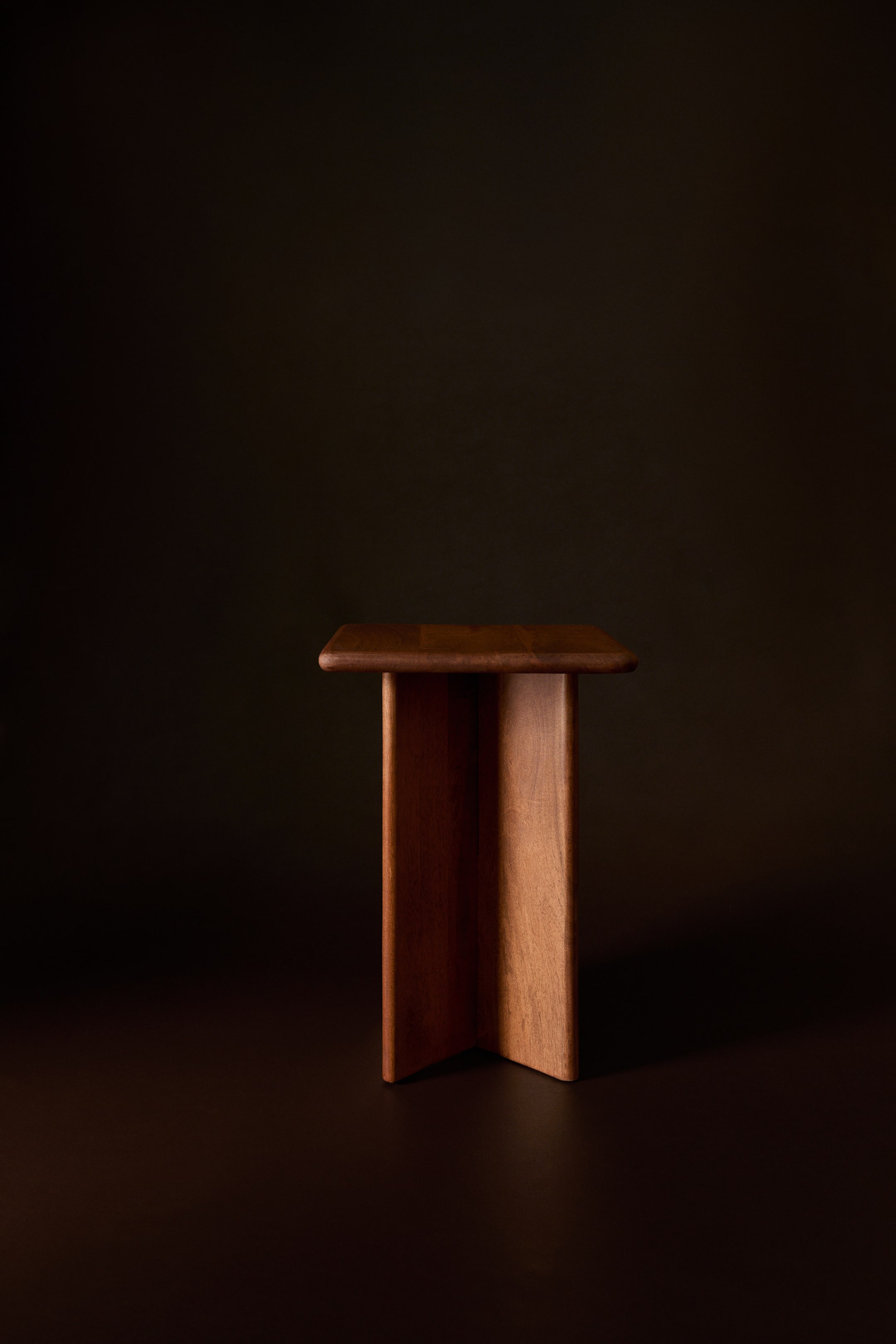 Größeres Bild ansehen: Ein quadratischer Beistelltisch aus Mangoholz ist aus einer frontalen Perspektive zu sehen und verfügt über eine flache, quadratische Tischplatte mit abgerundeten Kanten. Die Konstruktion wird von einem zentralen Sockelgestell getragen, das aus drei sich kreuzenden vertikalen Holzpaneelen mit sichtbar natürlicher Maserung besteht.