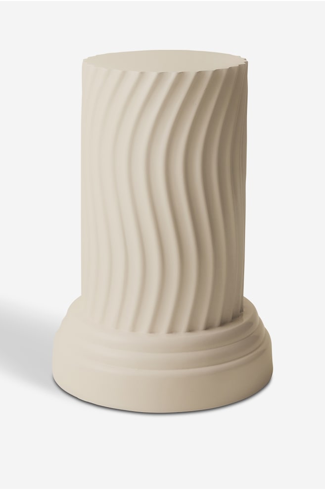 Une table sur pied de couleur crÃ¨me est debout, mettant en valeur un corps cylindrique ornÃ© de rainures verticales cannelÃ©es et ondulÃ©es. La structure repose sur une large base circulaire Ã  gradins, avec une finition mate et lisse. - 1