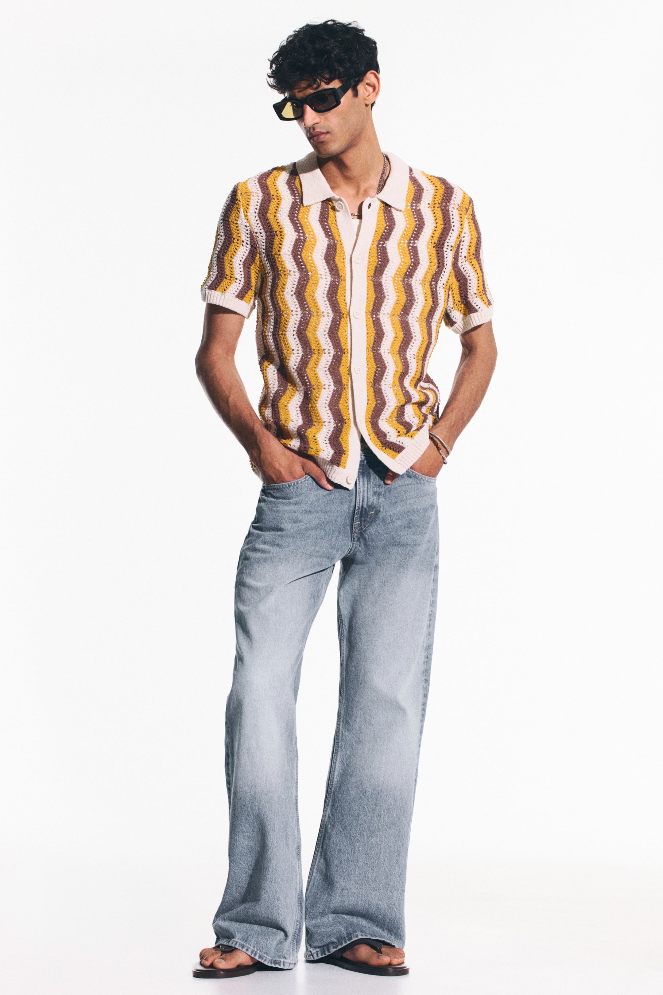View larger image: A knitted short-sleeved polo shirt, viewed from the front, showcases a zigzag pattern in white, mustard yellow, and brown. It features a polo collar and a full button-front placket.