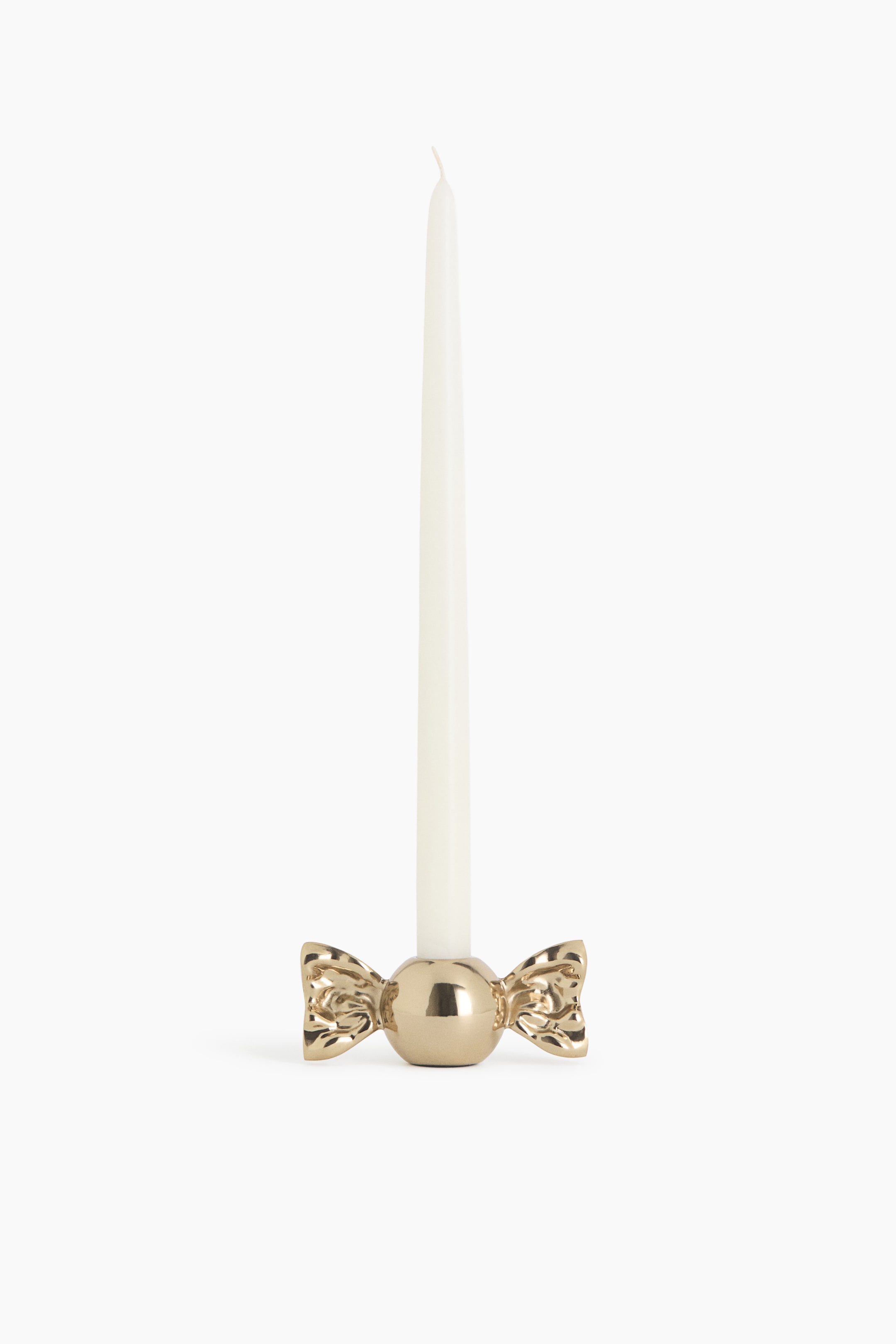 View larger image: A metallic gold candle holder designed in the shape of a wrapped candy is holding a tall, white taper candle. The front-facing holder features a glossy, polished finish with a smooth spherical centre and textured, flared wrapper details on both sides.