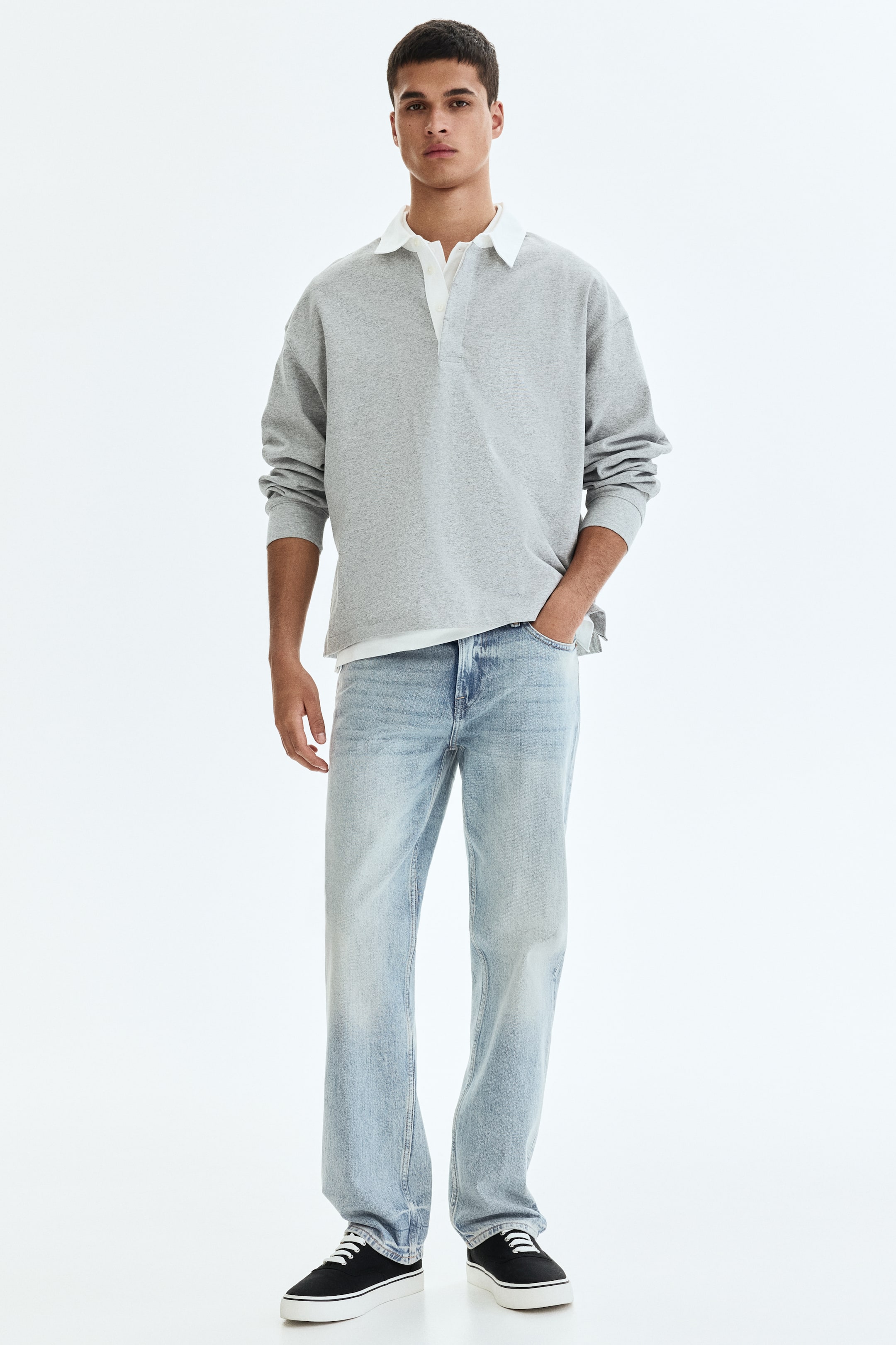 Grösseres Bild ansehen: Ein graues Langarm-Poloshirt wird aus einer Frontalansicht präsentiert, mit einem weißen Kragen und einer Knopfleiste. Ein weißer Unterhemdkragen schaut darunter hervor, und das Polo zeigt eine lockere Passform mit langen, geknöpften Ärmeln.