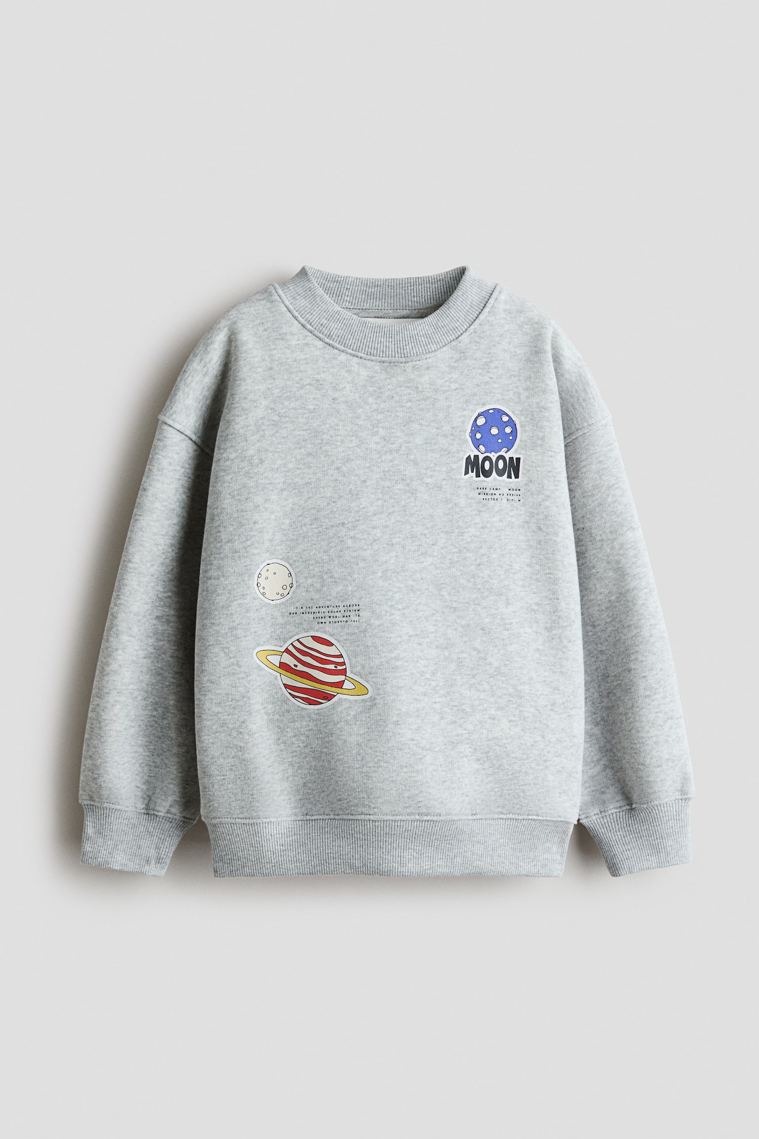 Má»t chiáº¿c sweatshirt mÃ u xÃ¡m nháº¡t melange ÄÆ°á»£c chá»¥p hÆ°á»ng chÃ­nh diá»n, ná»i báº­t vá»i phom dÃ¡ng rá»ng, vai trá» vÃ  bo gÃ¢n á» cá» Ã¡o, cá» tay vÃ  gáº¥u Ã¡o. Máº·t trÆ°á»c cÃ³ cÃ¡c há»a tiáº¿t in chá»§ Äá» khÃ´ng gian, bao gá»m má»t hÃ nh tinh mÃ u xanh vá»i chá»¯ "MOON" á» gÃ³c trÃªn bÃªn trÃ¡i vÃ  má»t hÃ nh tinh mÃ u Äá» cÃ³ sá»c kÃ¨m vÃ nh á» gÃ³c dÆ°á»i bÃªn pháº£i.