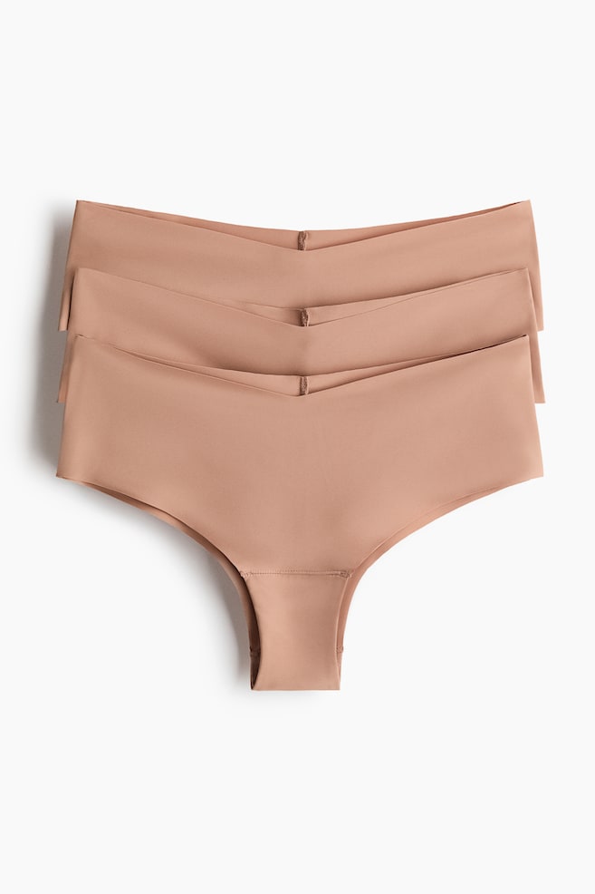 Drie huidkleurige microvezelslips liggen opgestapeld en tonen het vooraanzicht. Elk slipje heeft een lage, V-vormige taille, lasergesneden randen en uitgesneden zijkanten. - 1