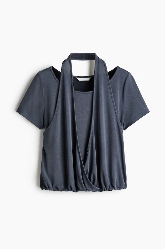A dark grey top is shown from the front, featuring short sleeves with cold-shoulder cutouts. The draped front panel crosses over the torso, forming a halter-style neckband and revealing a square-neck inner panel. An elasticated hem gathers the fabric at the bottom. - 1