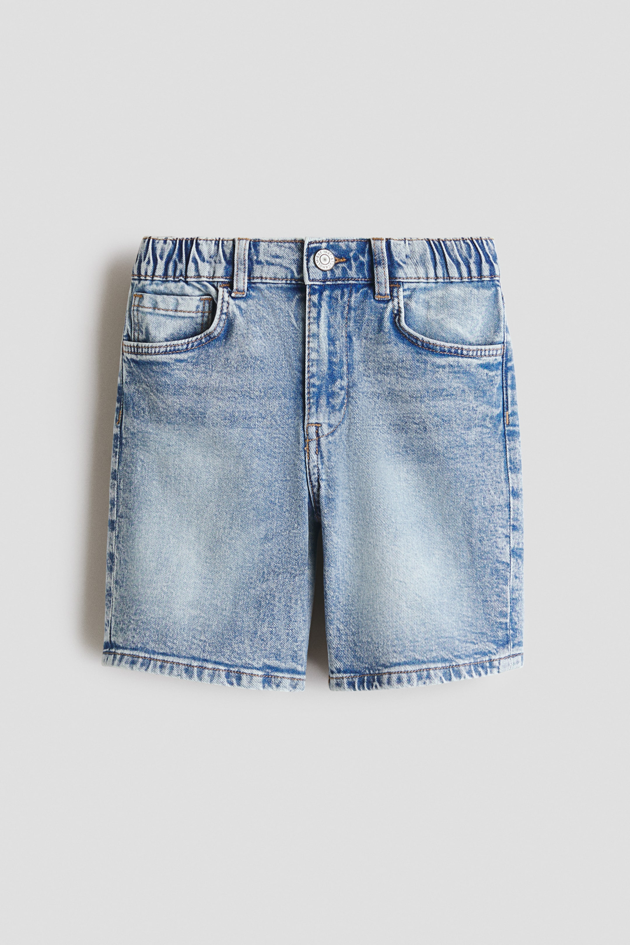 View larger image: Light blue denim shorts shown from the front, featuring a stone-washed finish. They come with a partially elasticised waistband with belt loops, a button closure, and front pockets including a coin pocket. The shorts are finished with a distressed hem.